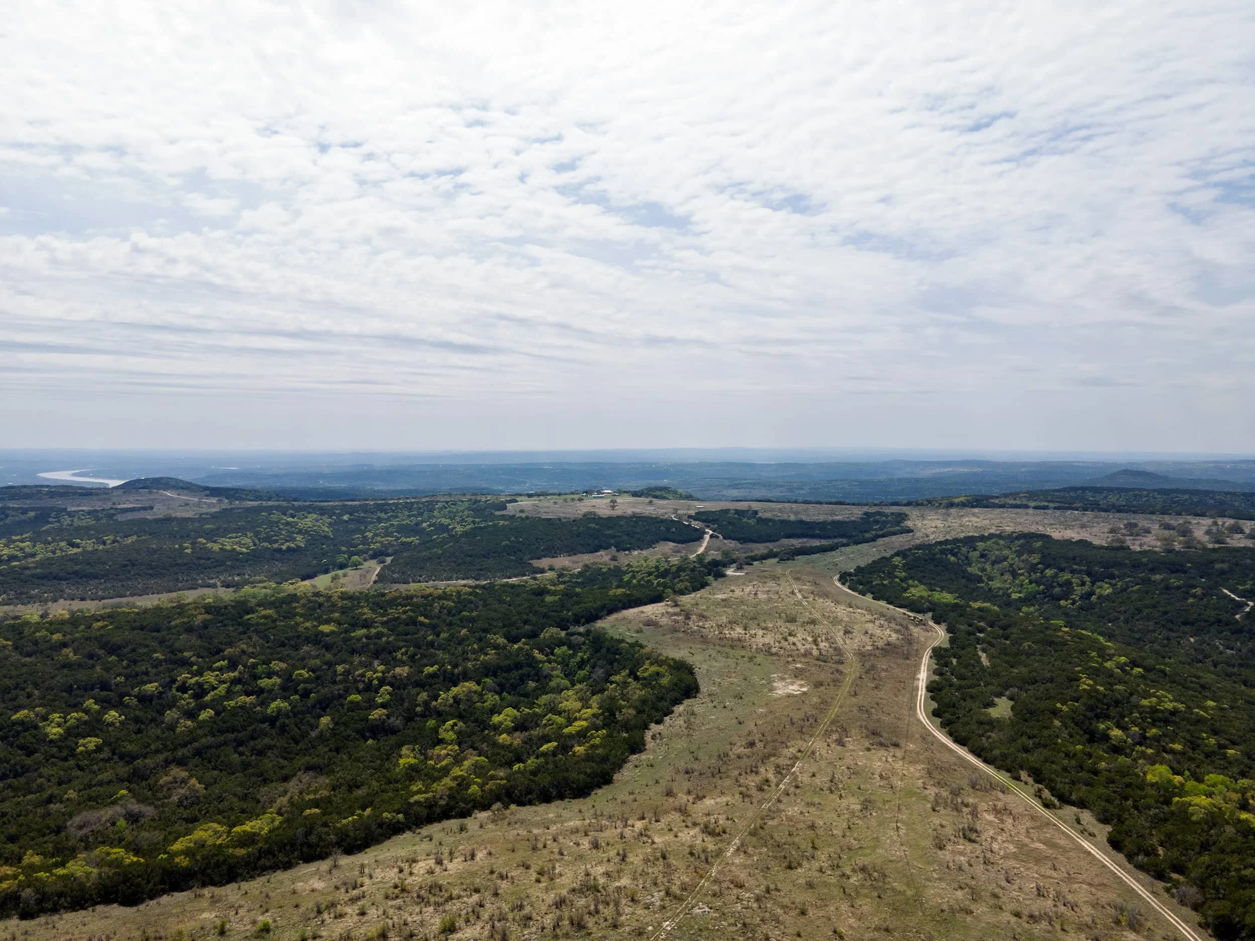 Aerial view of a landscape with a river, hills, and a partly cloudy sky.