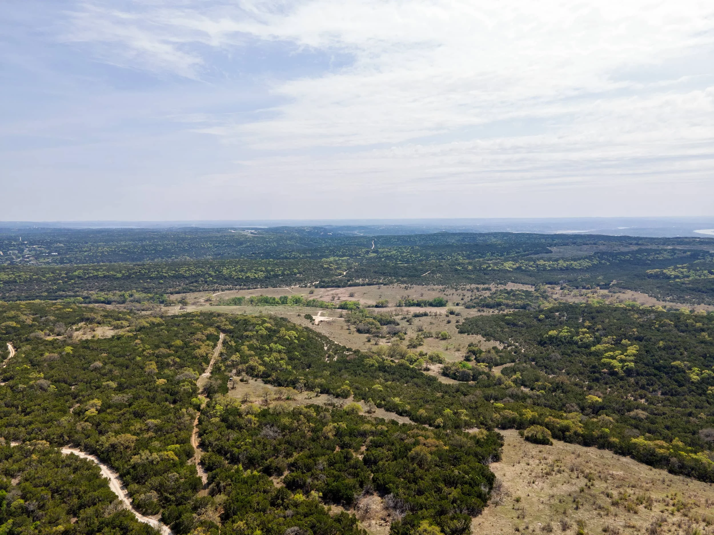 A vast landscape with green trees, a distant river or lake, and a partly cloudy sky overhead.
