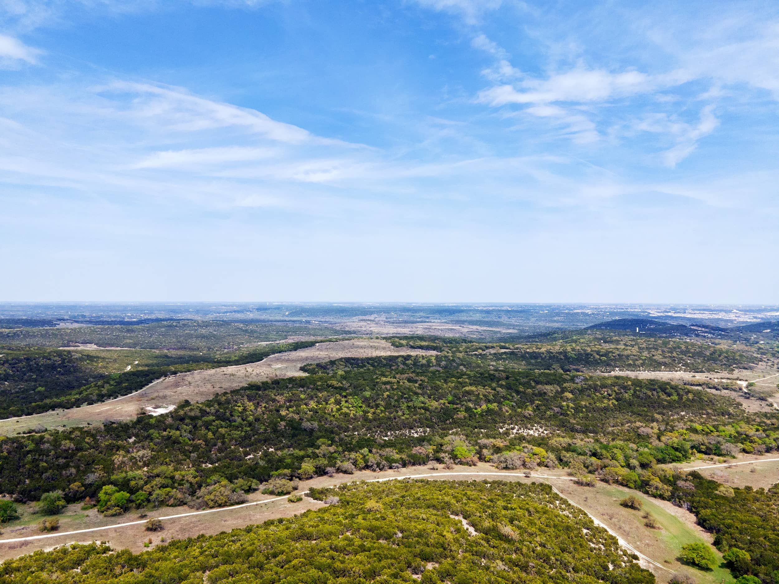A panoramic view of a landscape with rolling hills and trees, under a mostly cloudy blue sky.