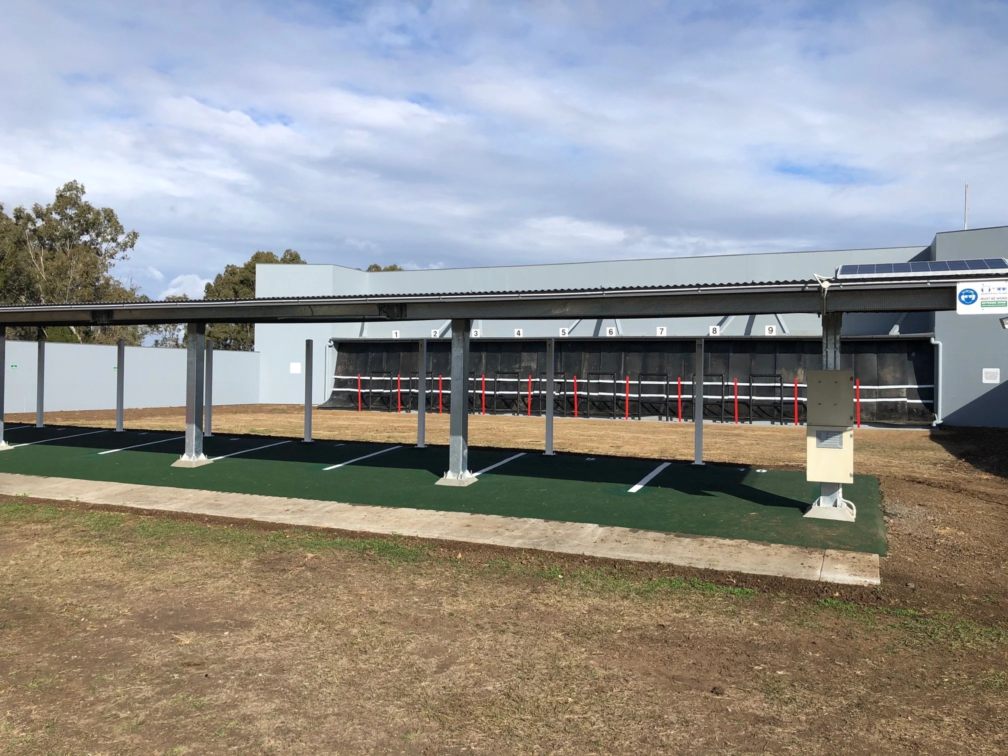 Construction of covered shooting range building with roof, open walls and green flooring