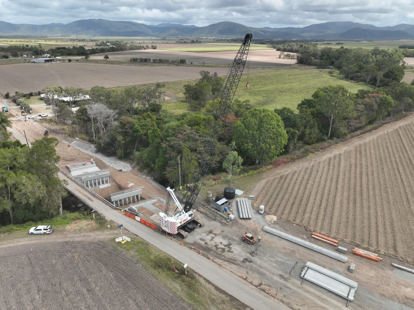 Drone image of regional road with construction on bridge and structure with machinery and trades people