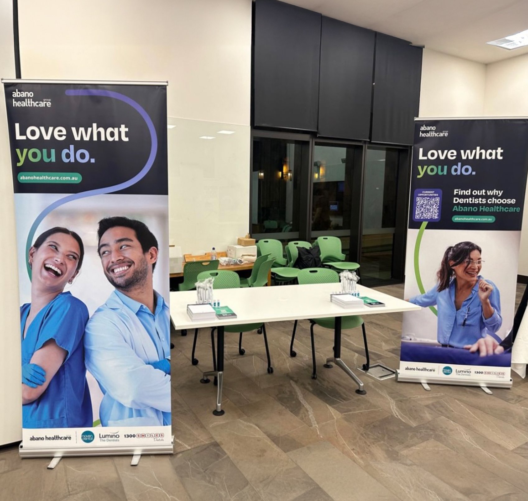 This image showcases an event setup for Abano Healthcare, emphasizing their refreshed brand identity. Two pull-up banners frame the scene, displaying the tagline "Love what you do" in bold typography, paired with vibrant brand colours and imagery of