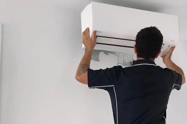 A man installing or servicing a wall-mounted air conditioner in a room with white walls.