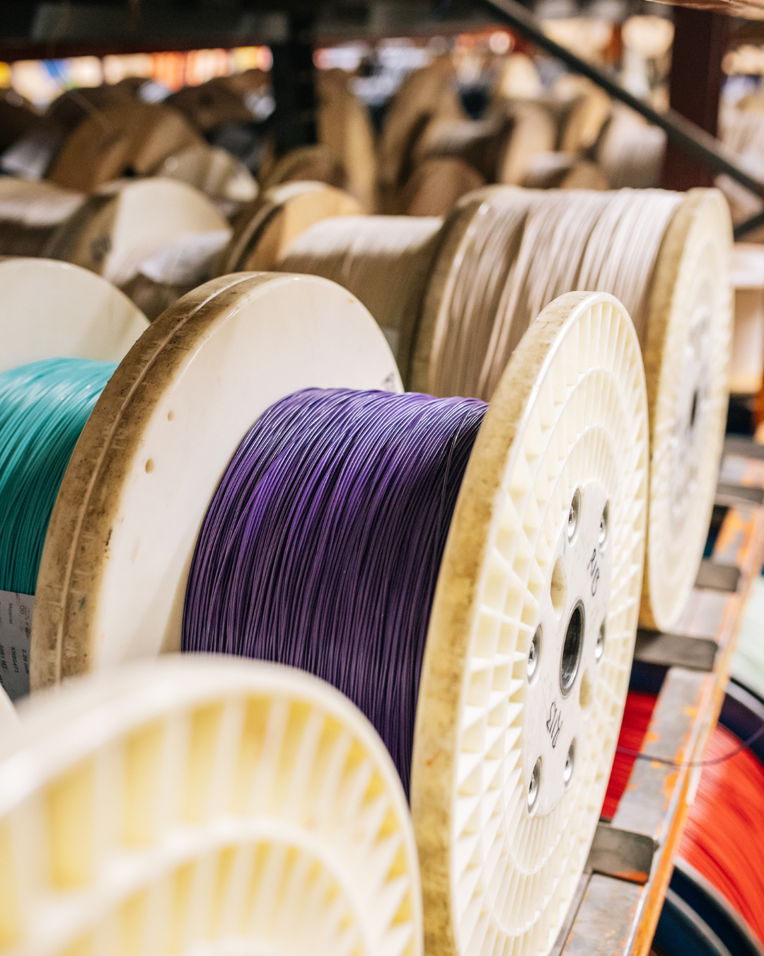 Spools of colorful filament on a storage rack in a workshop.