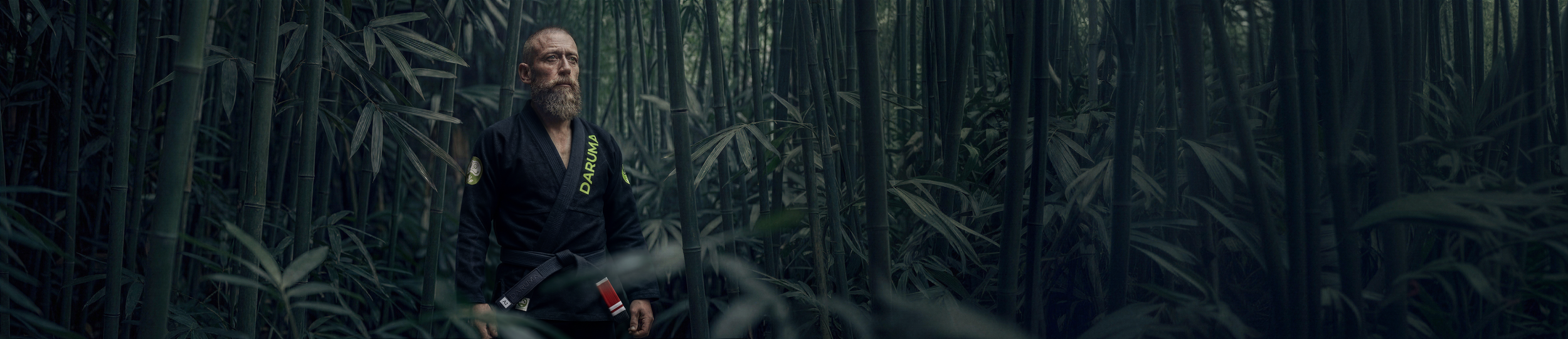 A man with a beard dressed in a black 100% Hemp Gi uniform standing in a dense bamboo forest.