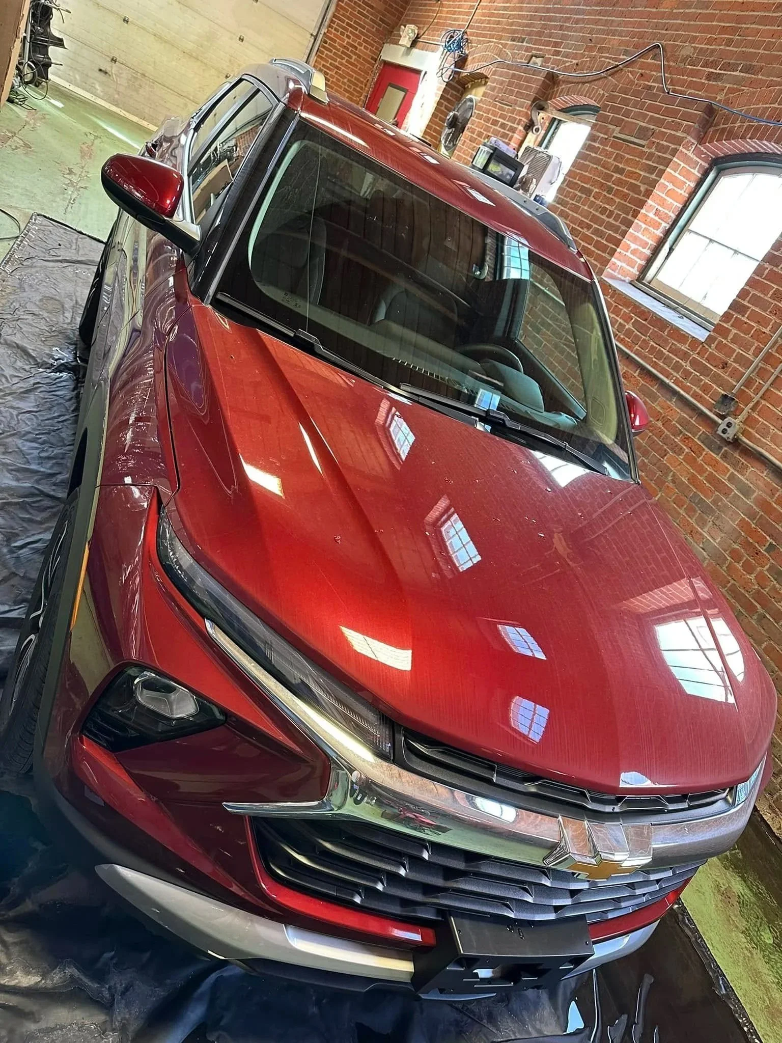 Red Chevrolet SUV inside a garage with brick walls, reflecting windows and ceiling lights getting detailed at Apex Detailing Co. in New Milford, CT.