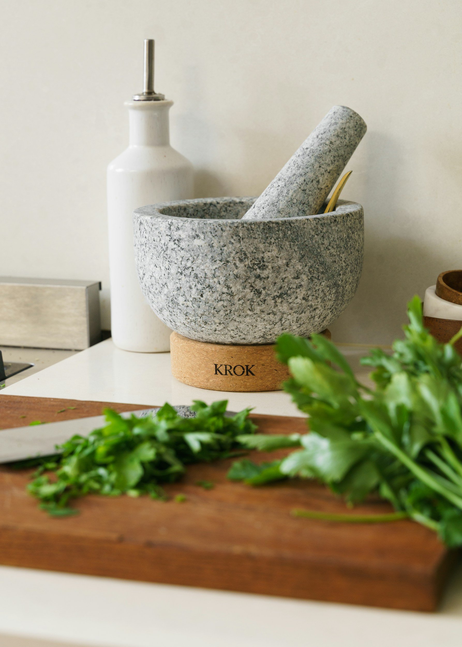 A marble mortar and pestle, a bottle of substance, and chopped herbs on a cutting board.