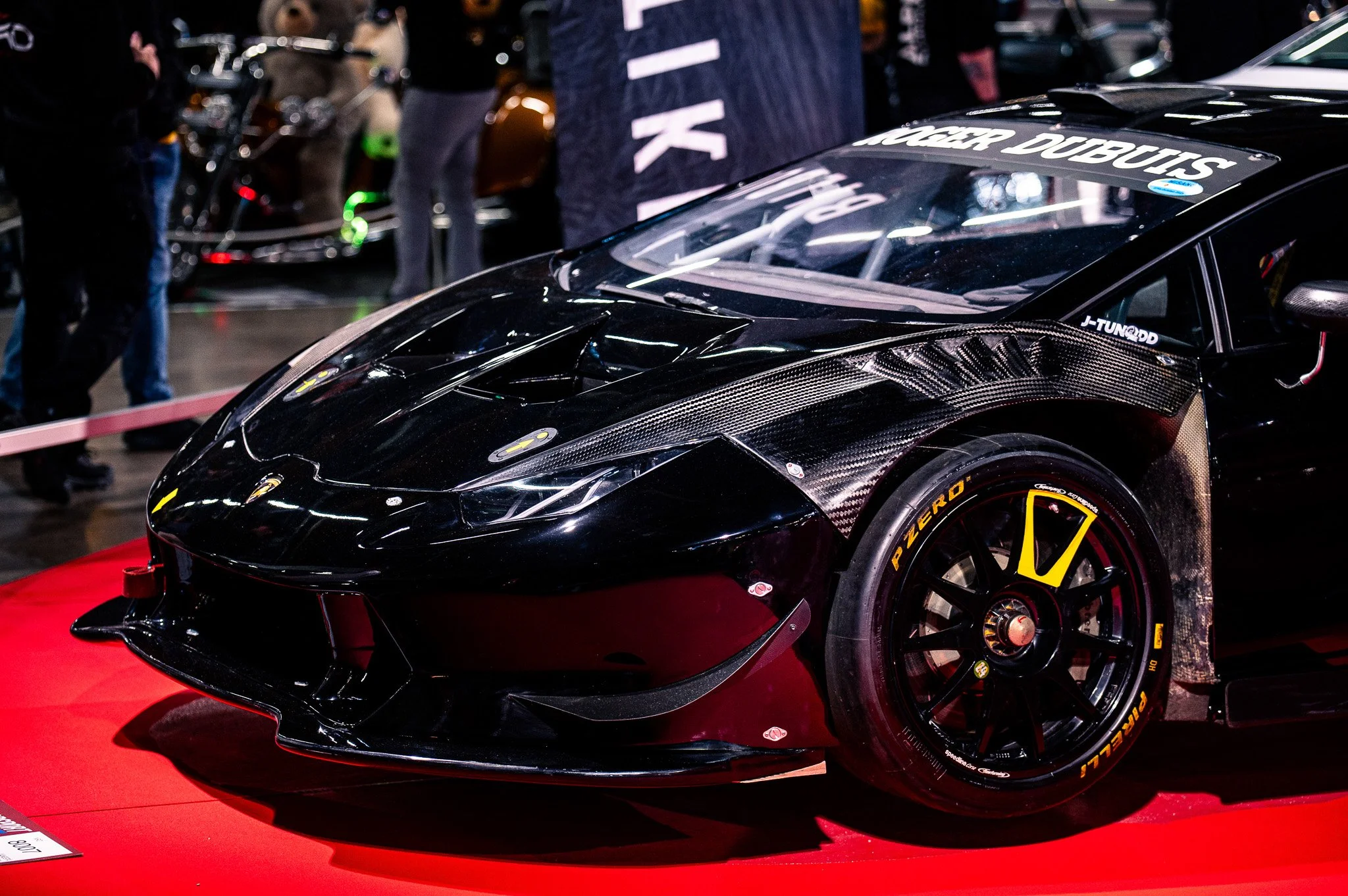 Mustavalkoinen urheiluauto autonäyttelyssä, kiiltävä ja high-tech-tyylinen, istuu punaisella alustalla.