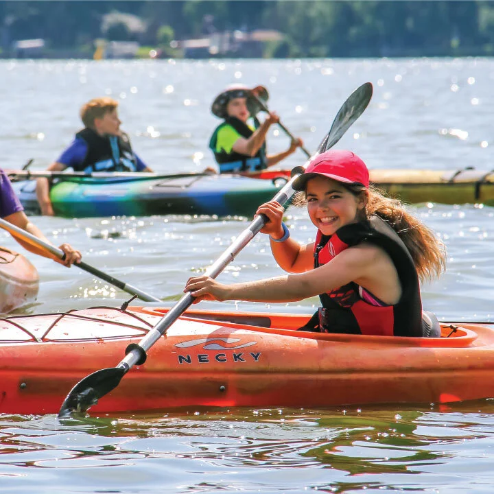  Summer photo of a girl kayaking in an orange kayak.  