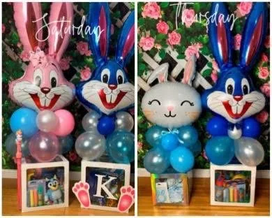 A Tuffy-themed balloon arrangement, featuring a large Tuffy character balloon on top, surrounded by blue and silver smaller balloons, with pink roses and green foliage in the background, and a box containing Tuffy-themed party favors at the bottom.