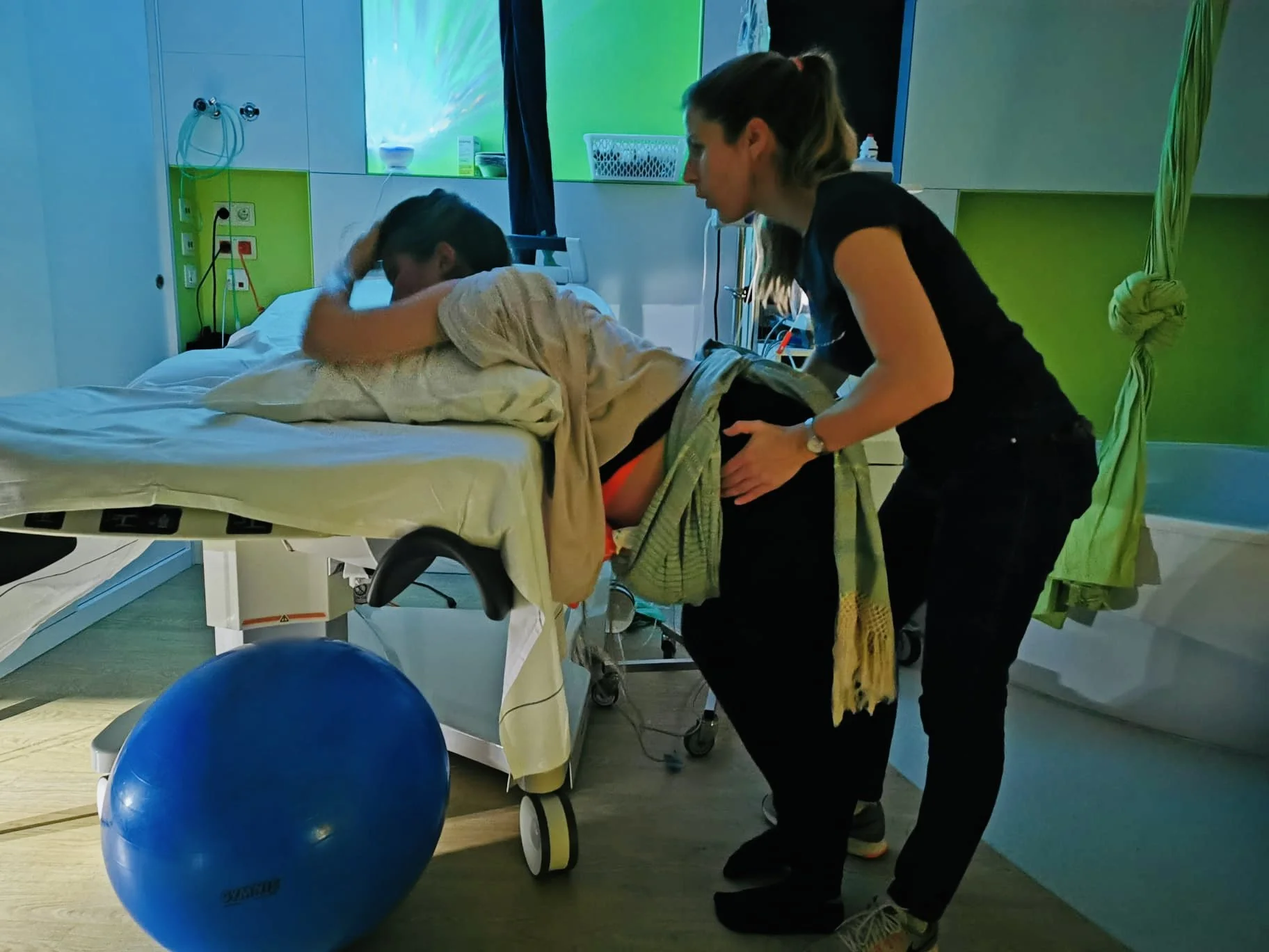Une jeune fille en train d'être aidée par une professionnelle dans un hôpital, probablement pour une rééducation, avec un ballon bleu placé à côté d'eux.