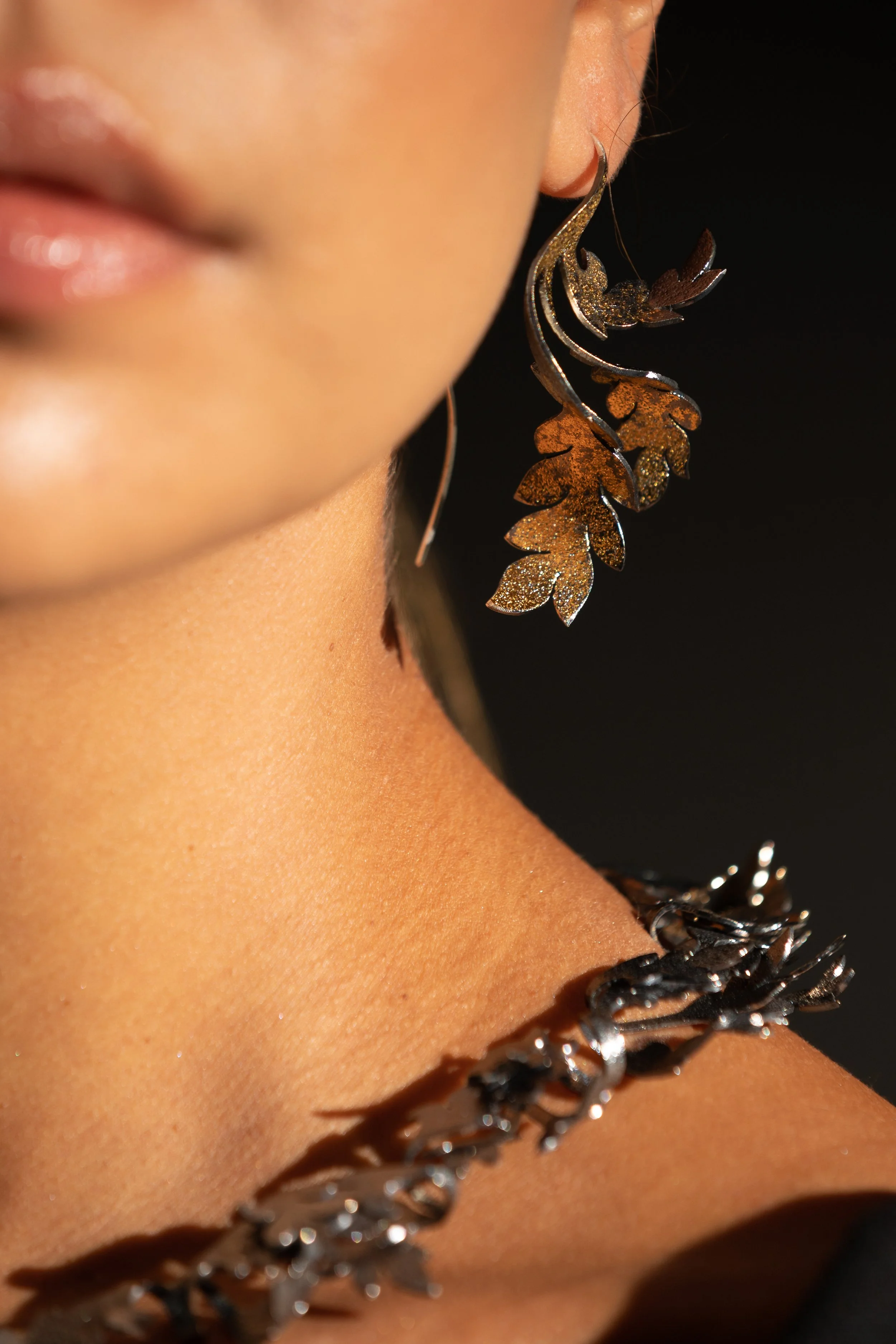 Close-up of a woman wearing leaf-shaped earrings and a necklace, with smooth skin and partially visible lips.