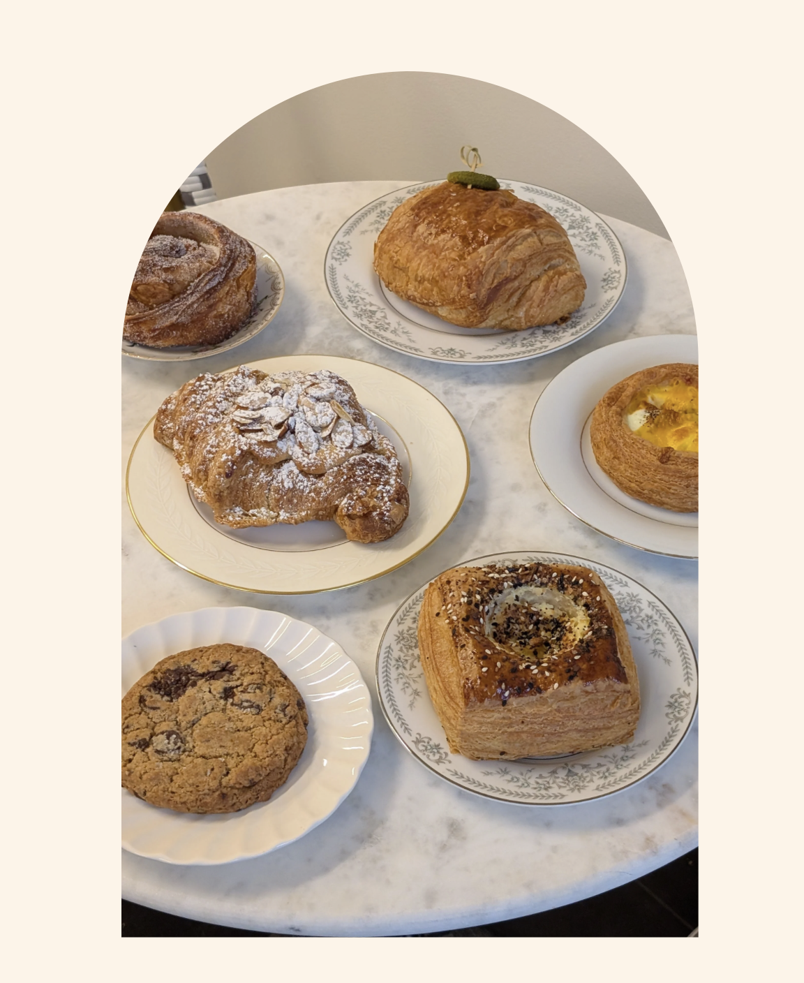 Assorted pastries on a white marble table, including a croissant, a cinnamon roll, a cookie, and other baked goods.