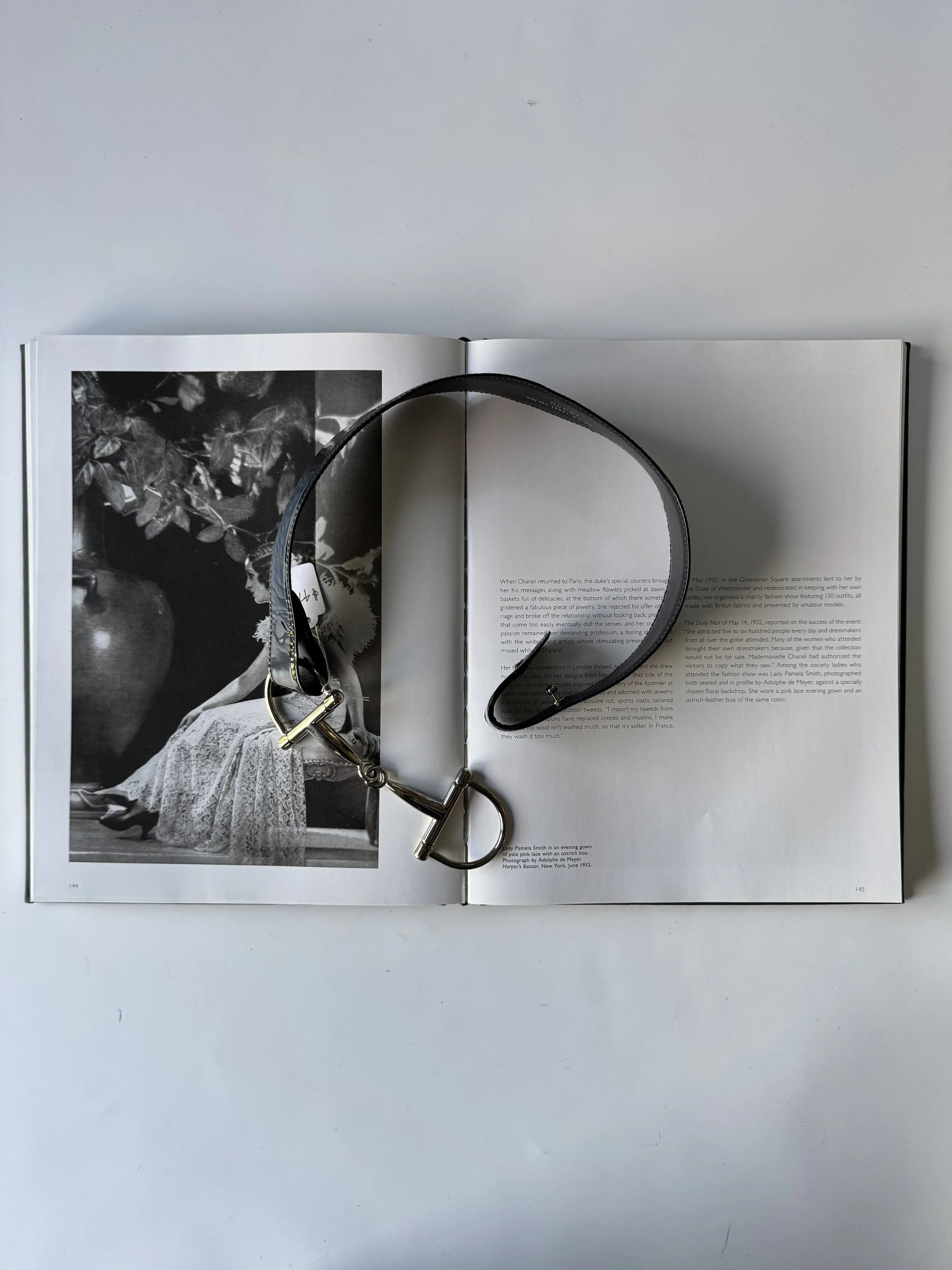 Open book with black and white photograph of a woman in a lace dress on the left page, and text on the right page, with a black leather strap with a metal clasp laying across both pages.