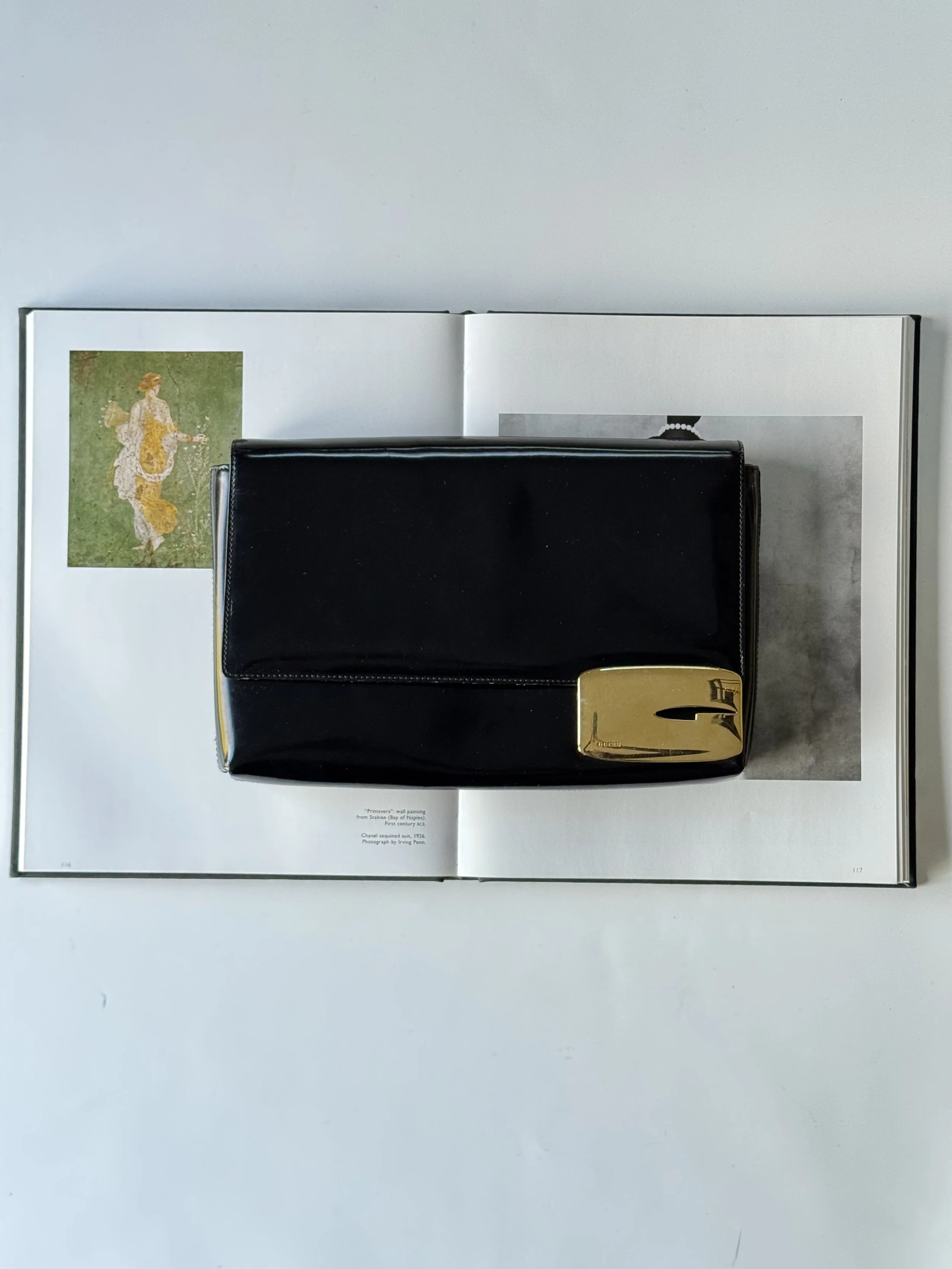 Open book with a painting of a woman on the left page and a black purse with a gold clasp on top of the right page.