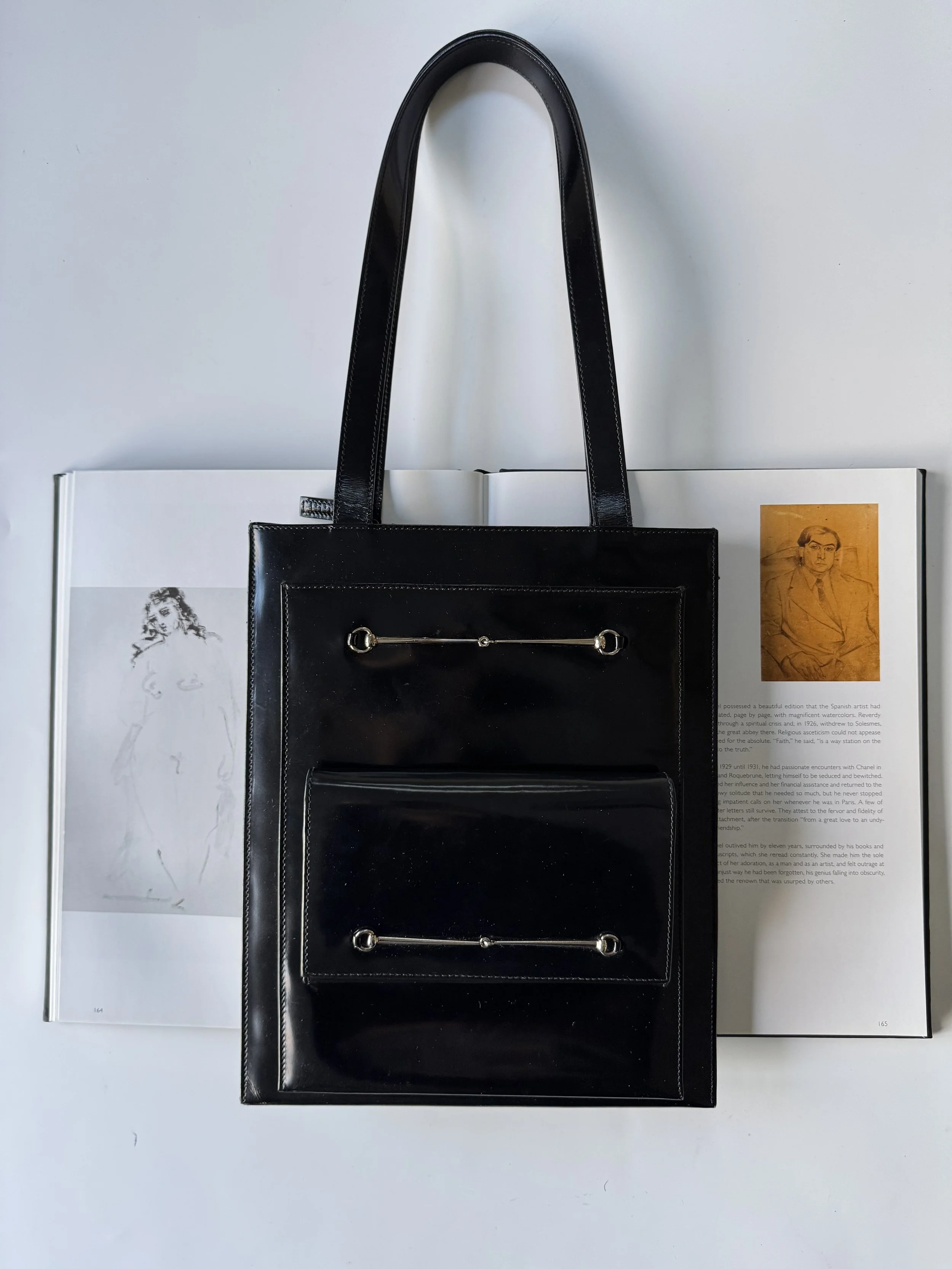 Black handbag with metal accents, placed on an open magazine or book with black-and-white and colored photographs.