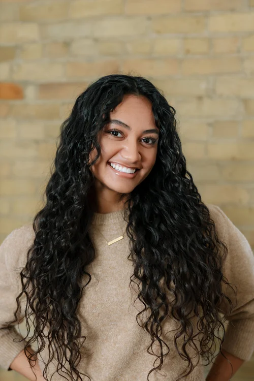 Salomé White, with long curly black hair and a beige sweater.