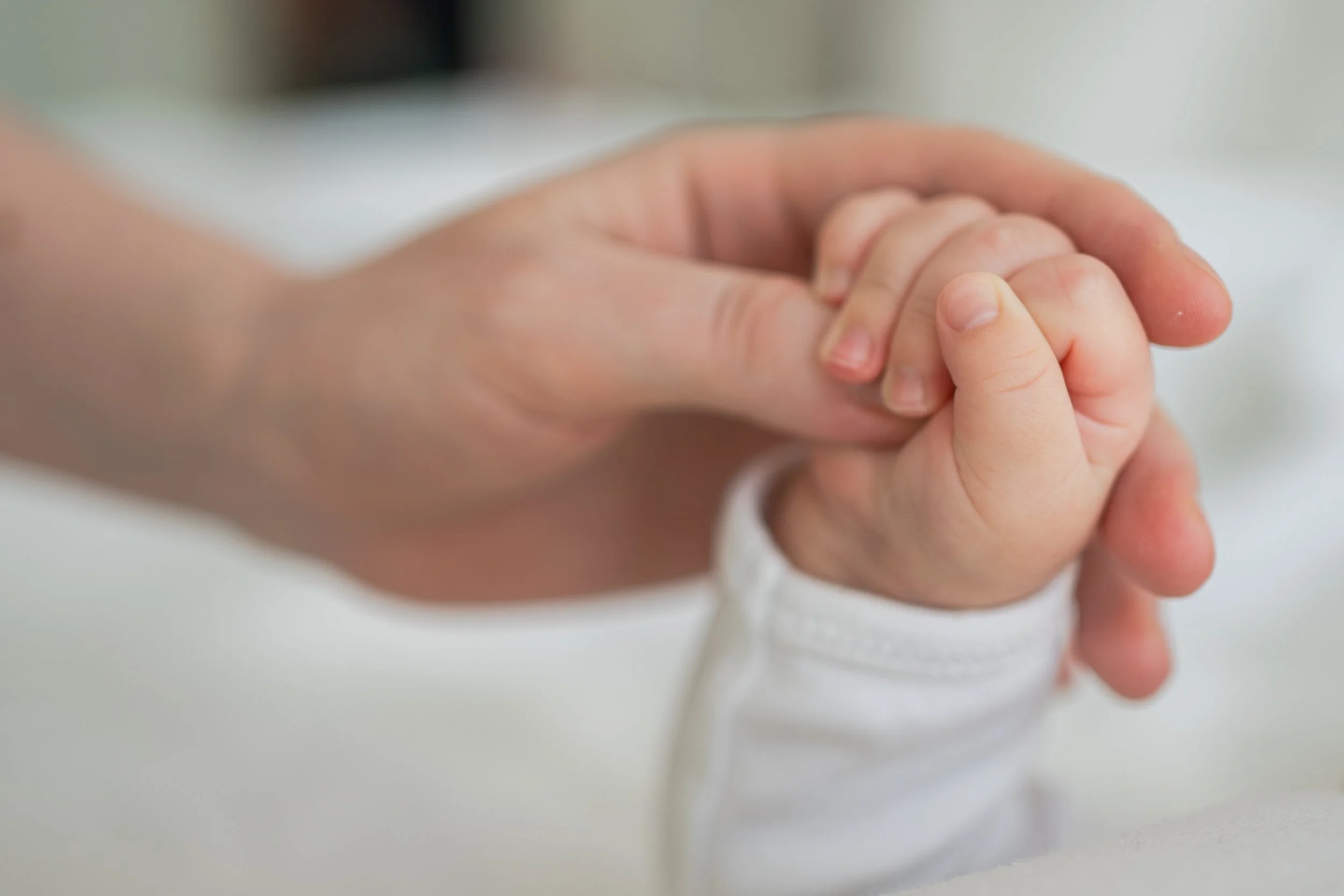 Close-up of a parent holding a baby’s hand, symbolizing the emotional bond and vulnerability of new parenthood.