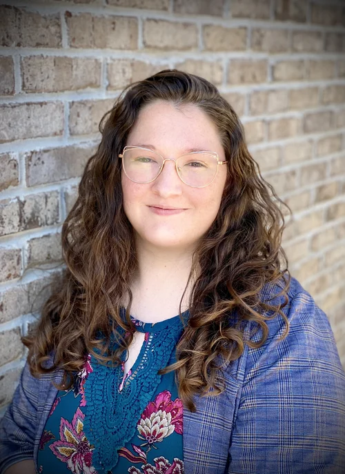 Ariel DeBardelaben, with curly brown hair and glasses.