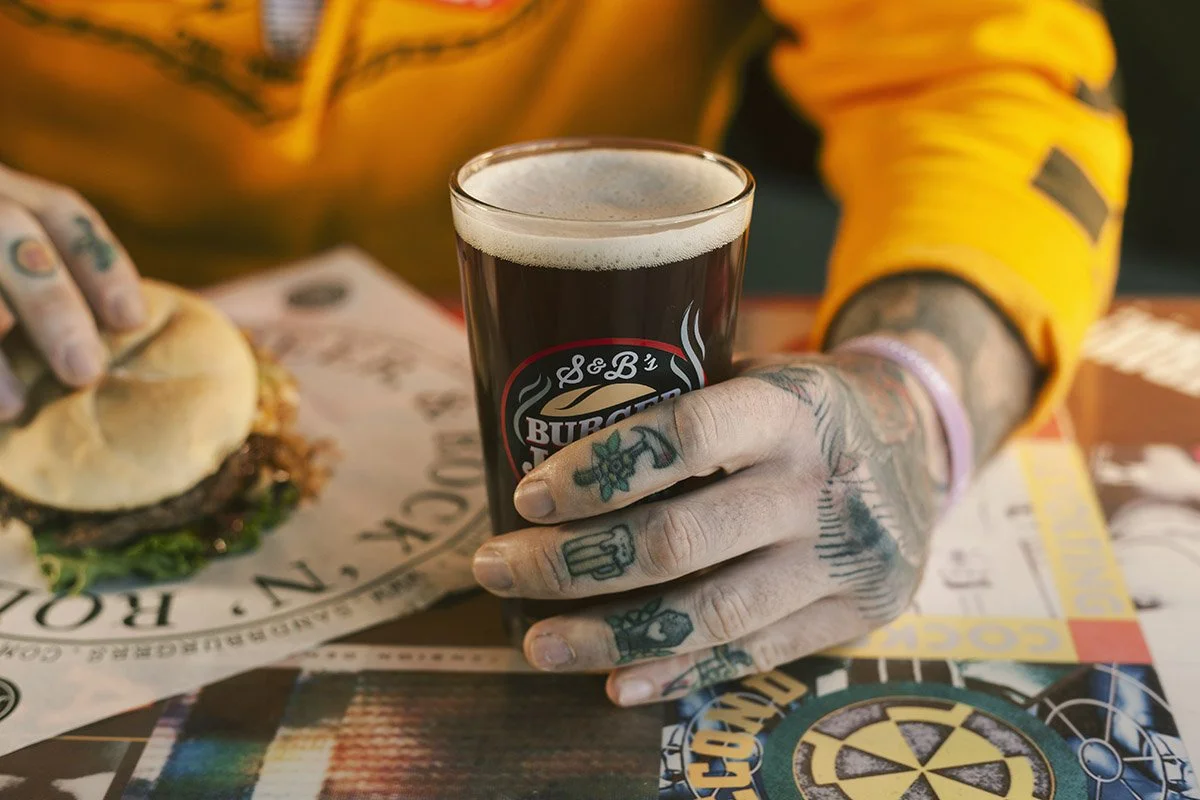 Tattooed hands enjoying a cold beer and a burger.