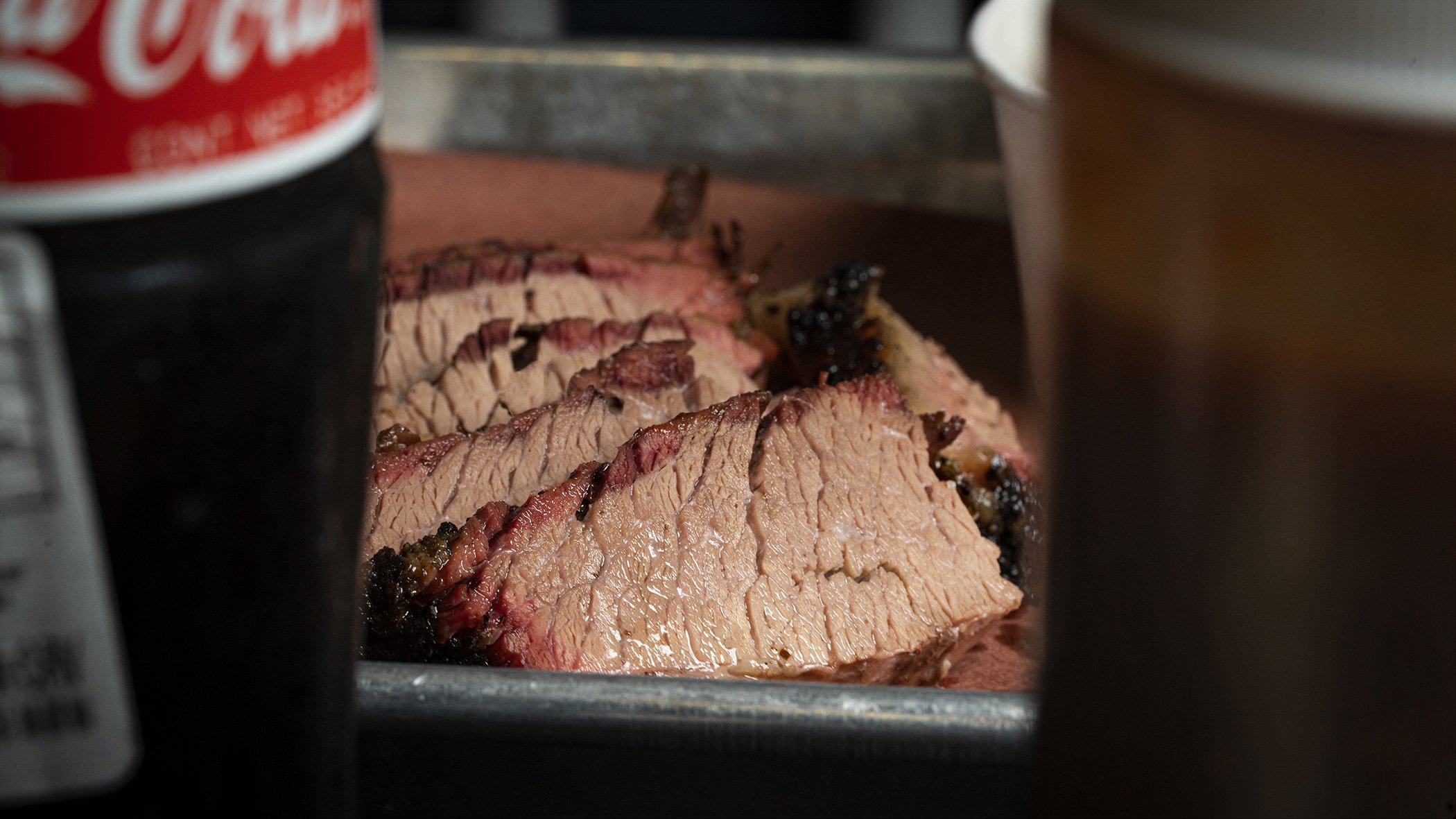 Slices of cooked steak on a cutting board, partially visible Coca-Cola can on the left, and another beverage container on the right.