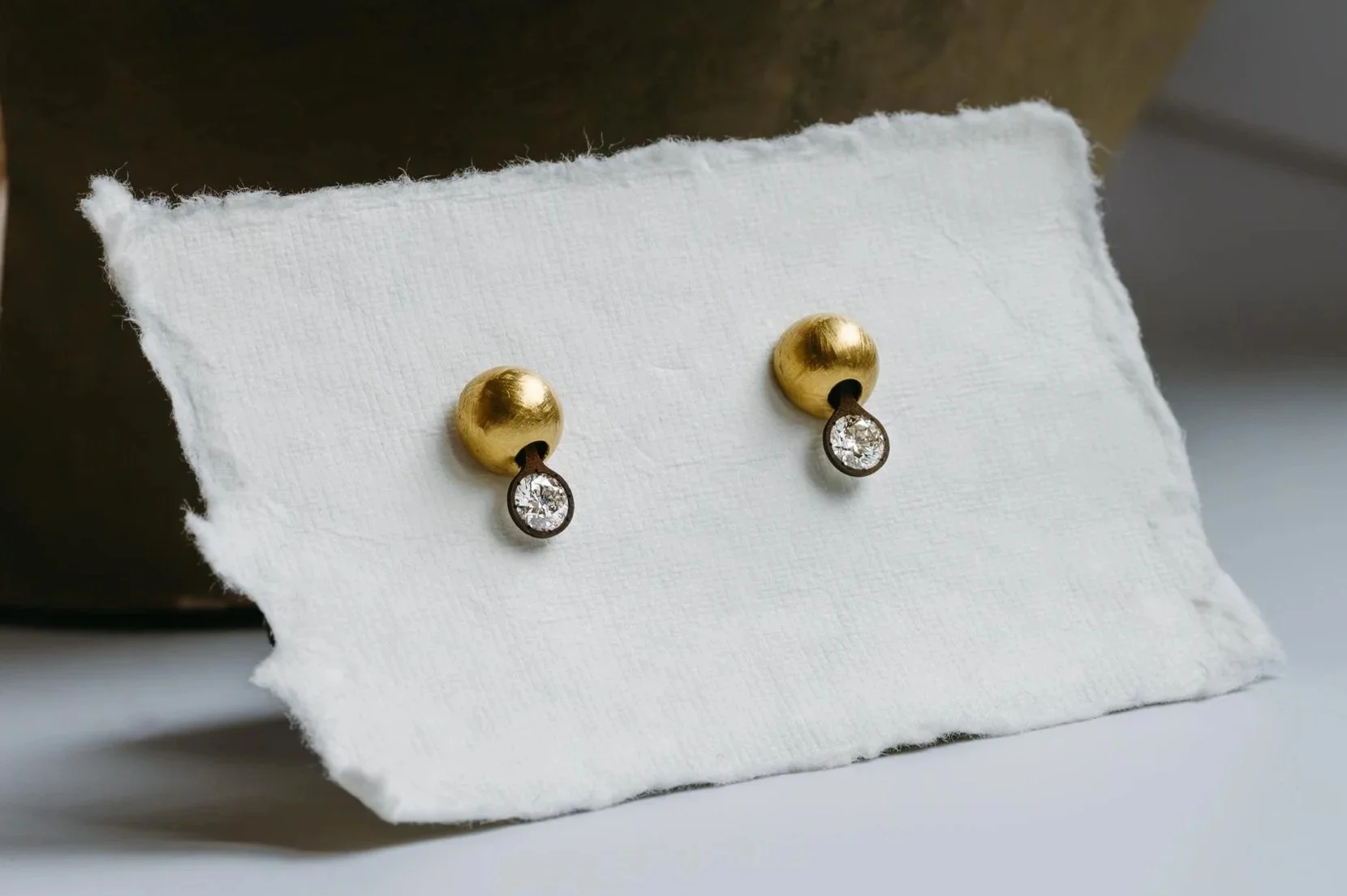 Gold stud earrings with dangling clear gemstones displayed on white textured fabric