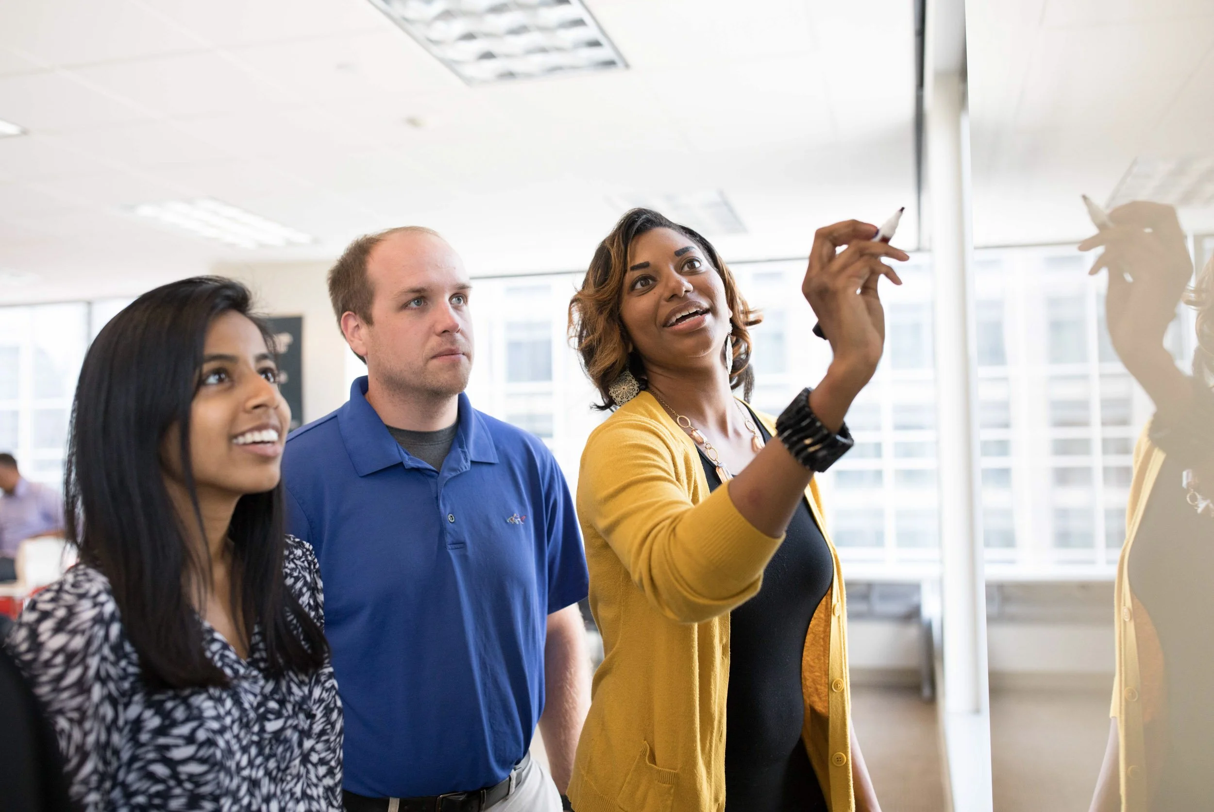 A man giving a presentation at a conference, with a screen behind him displaying the text "Kingdom Advisors Champions Forum New York." Several seated attendees listen, some taking notes, in a modern conference room.