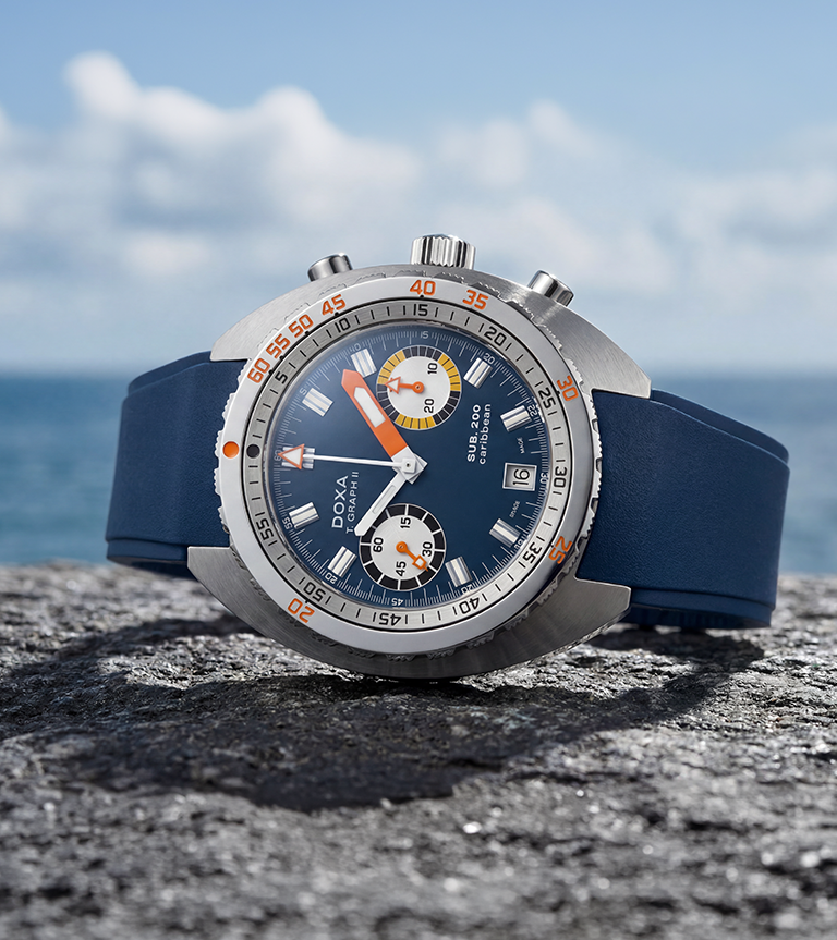 A Doxa SUB 200 T Graph II professional dive watch with a blue dial and rubber strap on top of a cliff with ocean background.
