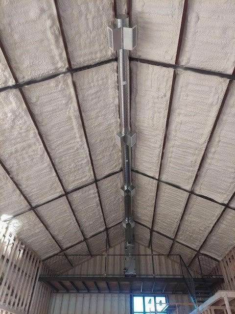 Insulated ductwork running along ceiling inside building with exposed framing.