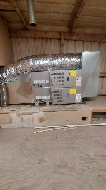 HVAC air handler unit installed in a wooden shed with a flexible duct attached.