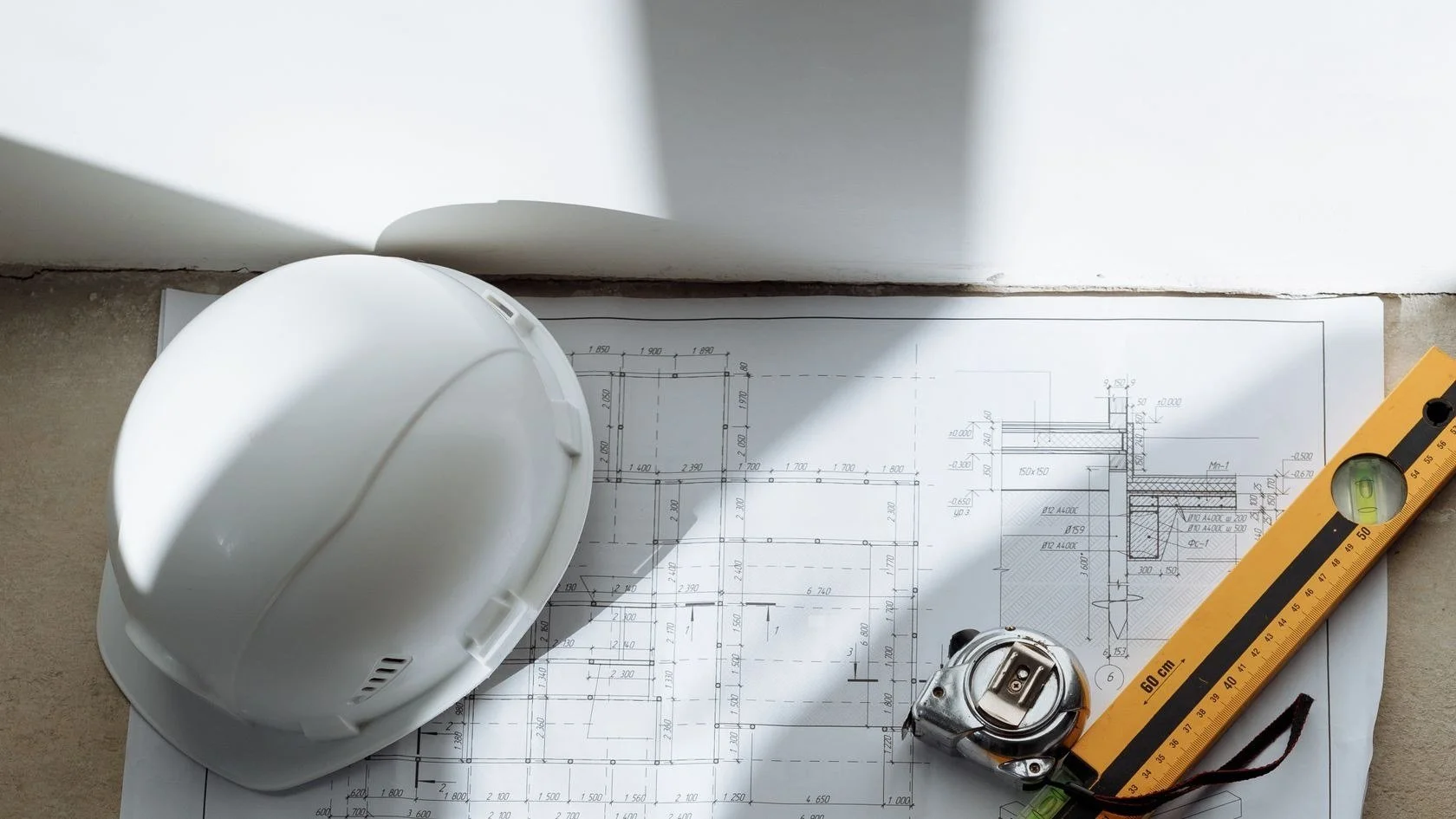 Construction drawings with a white hard hat, tape measure and level used to prepare a detailed telecom scope of work