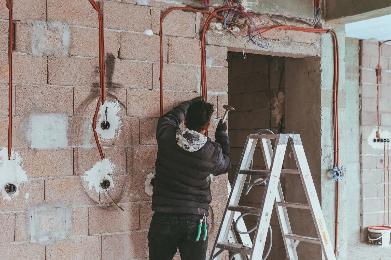 Installer on a ladder roughing in conduit and outlet box locations on a masonry wall before finishes