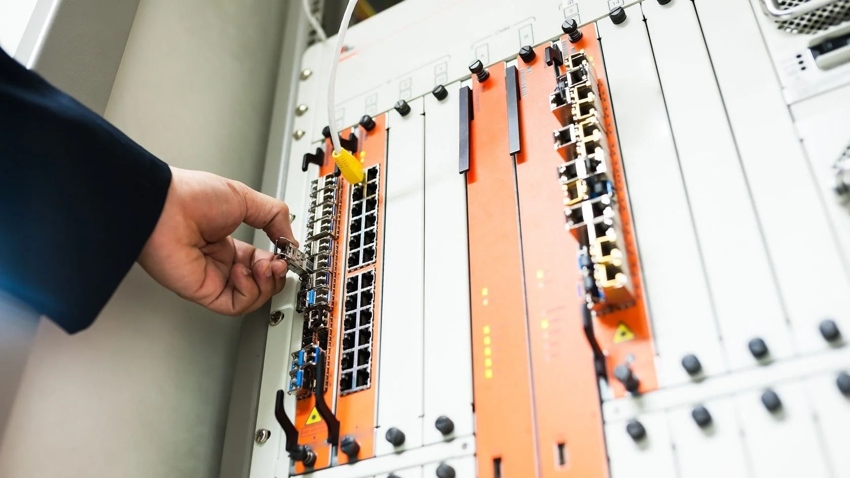 Technician connecting cabling to high-capacity line cards with fiber and copper ports in a telecom equipment chassis