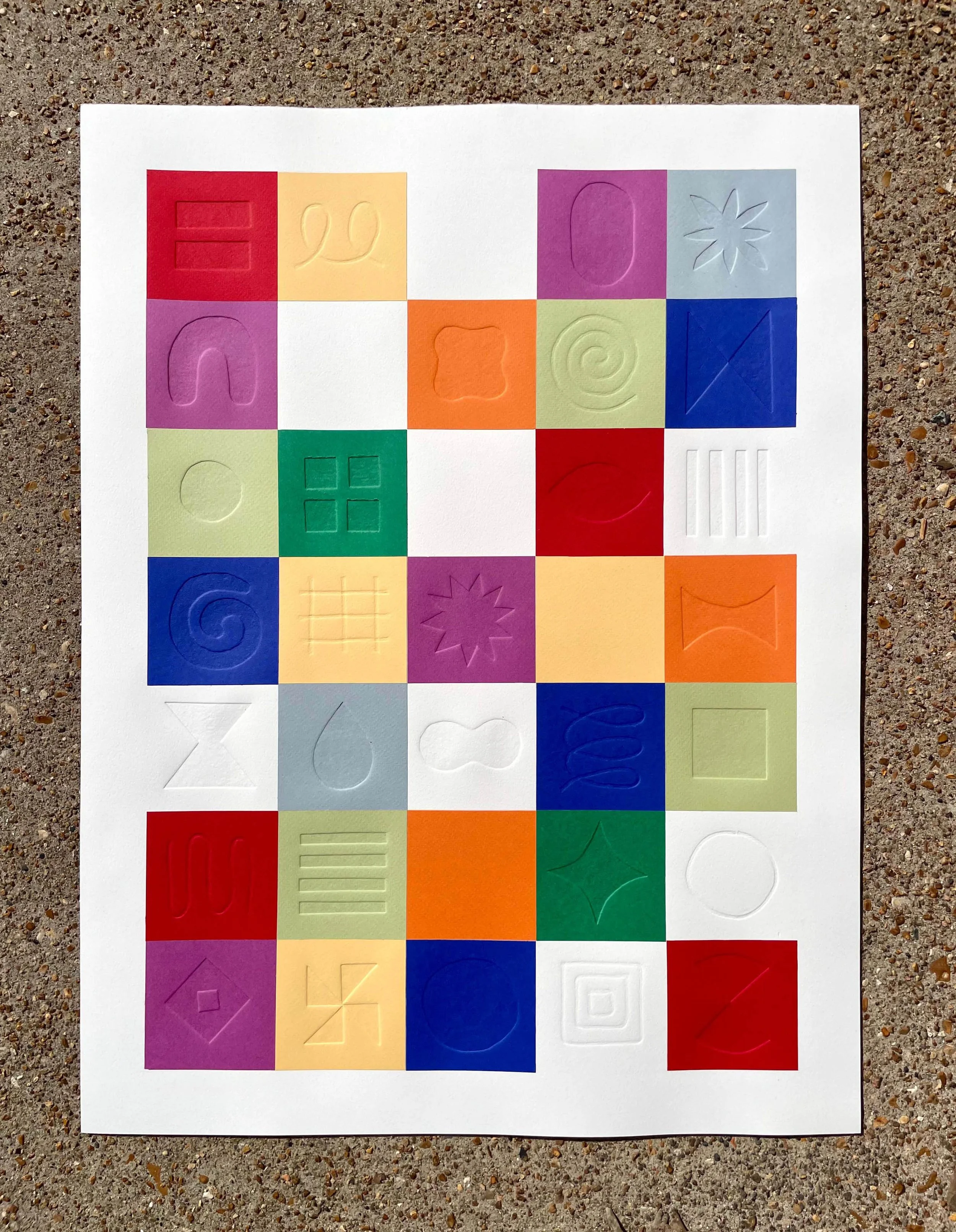 Colorful paper tiles with embossed symbols arranged in a grid on a white background placed on the ground.