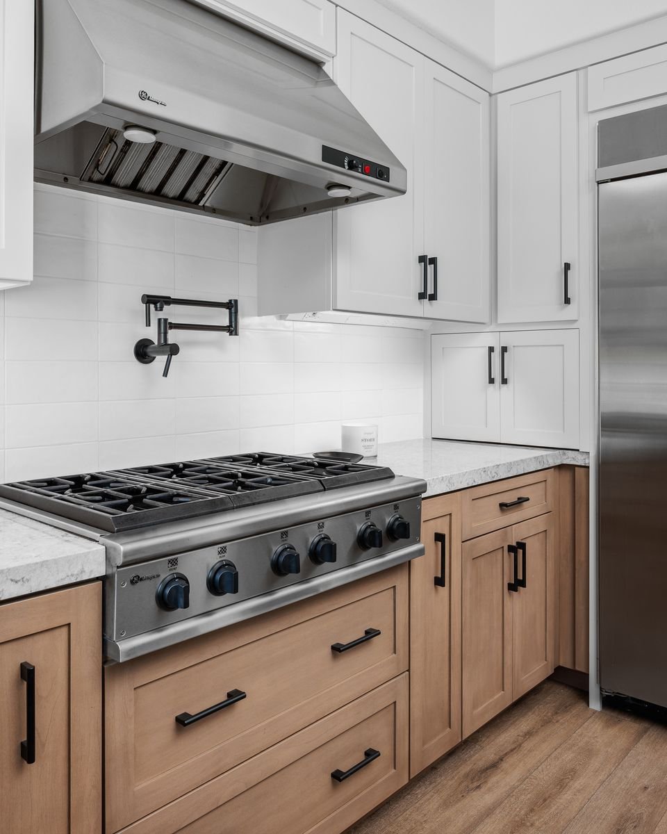 Modern kitchen with a stainless steel gas stove, wooden cabinets, pot filler, stainless steel range hood, and white tiled backsplash.