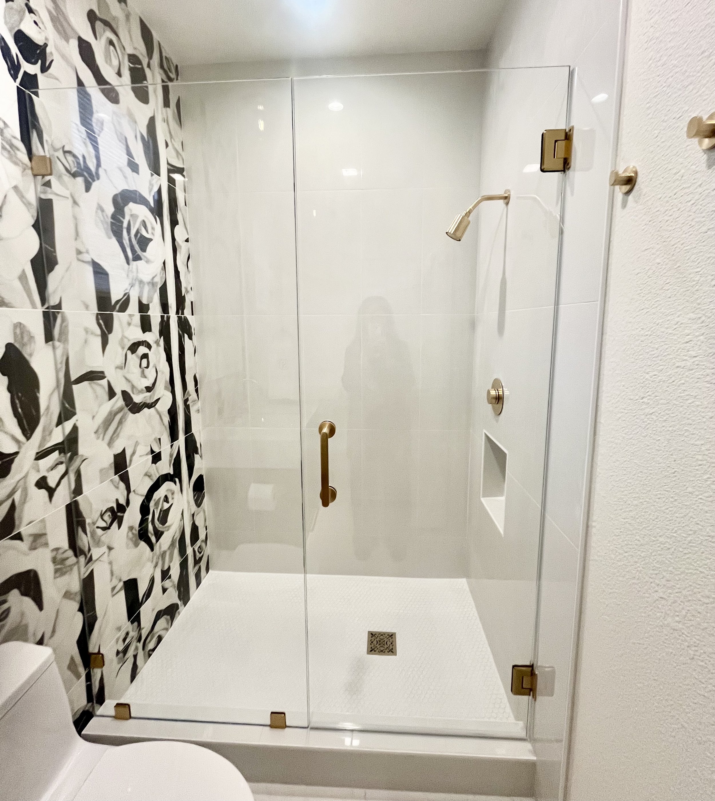Modern bathroom with glass shower enclosure, floral wall tiles, and white fixtures.