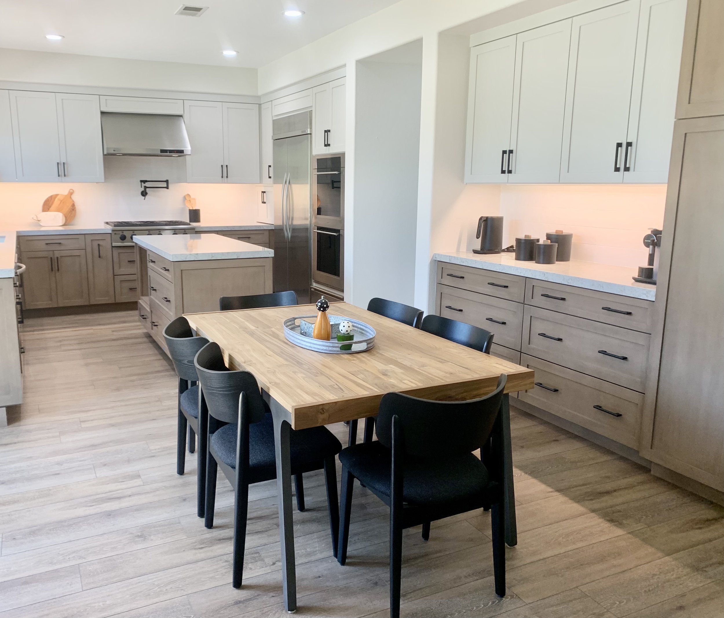 Modern kitchen with light wood cabinetry, center island, dining table with black chairs, stainless steel appliances, and wood flooring.