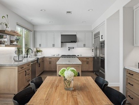 Modern kitchen with wooden dining table, black chairs, stainless steel appliances, white cabinets, and a central island.