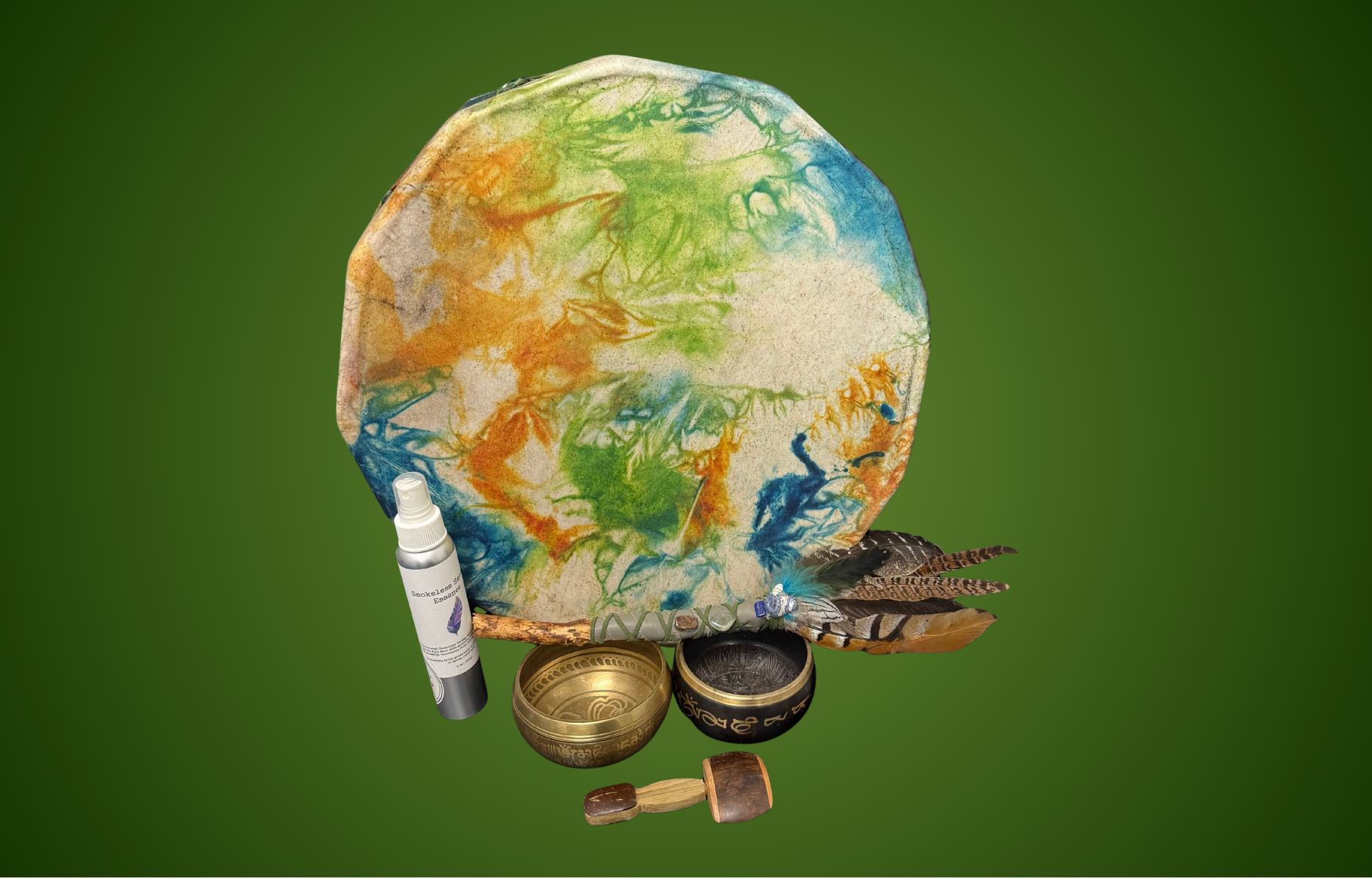 A colorful tie-dye fabric with feathers, small bowls, a spray bottle, and a small wooden object on a green background.