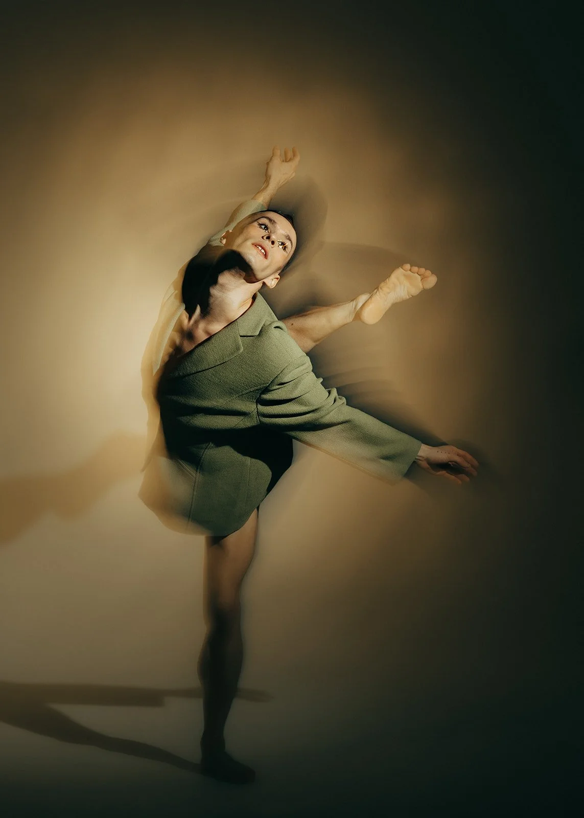 A man in a business suit performing a ballet pose with one leg raised and arms extended against a gradient background.