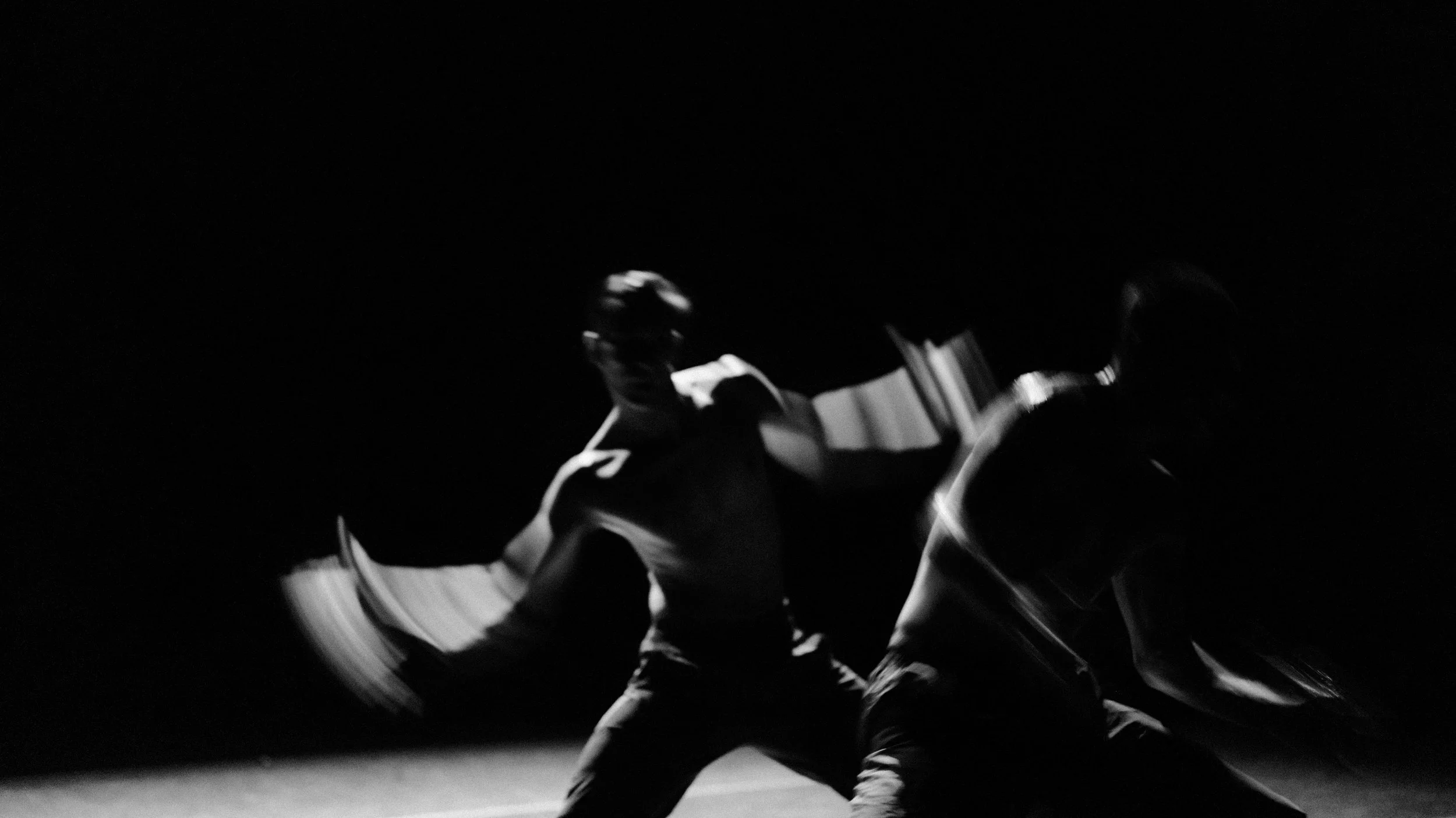 A person dancing in a dark setting, illuminated by a light source creating dynamic shadows and highlights.