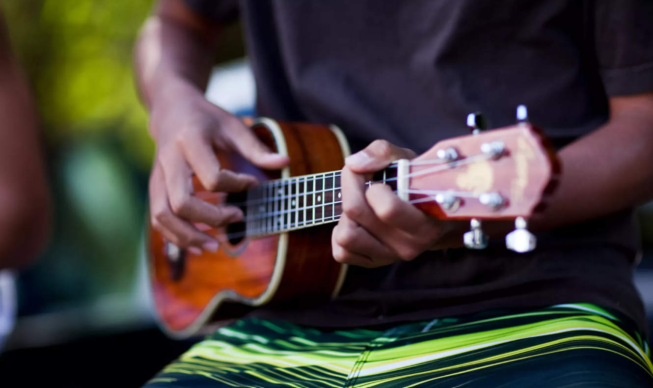 Close-up of musician playing Hawaiian ukulele, fingers on fretboard, highlighting traditional island music and cultural performance.