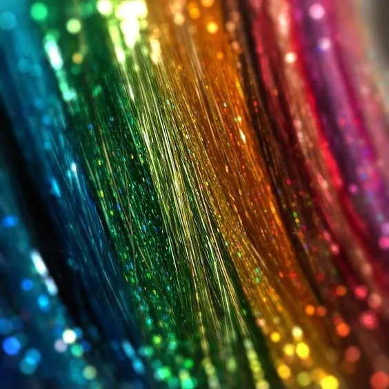 Close-up of colorful glittery strands arranged in a rainbow pattern from blue to pink.
