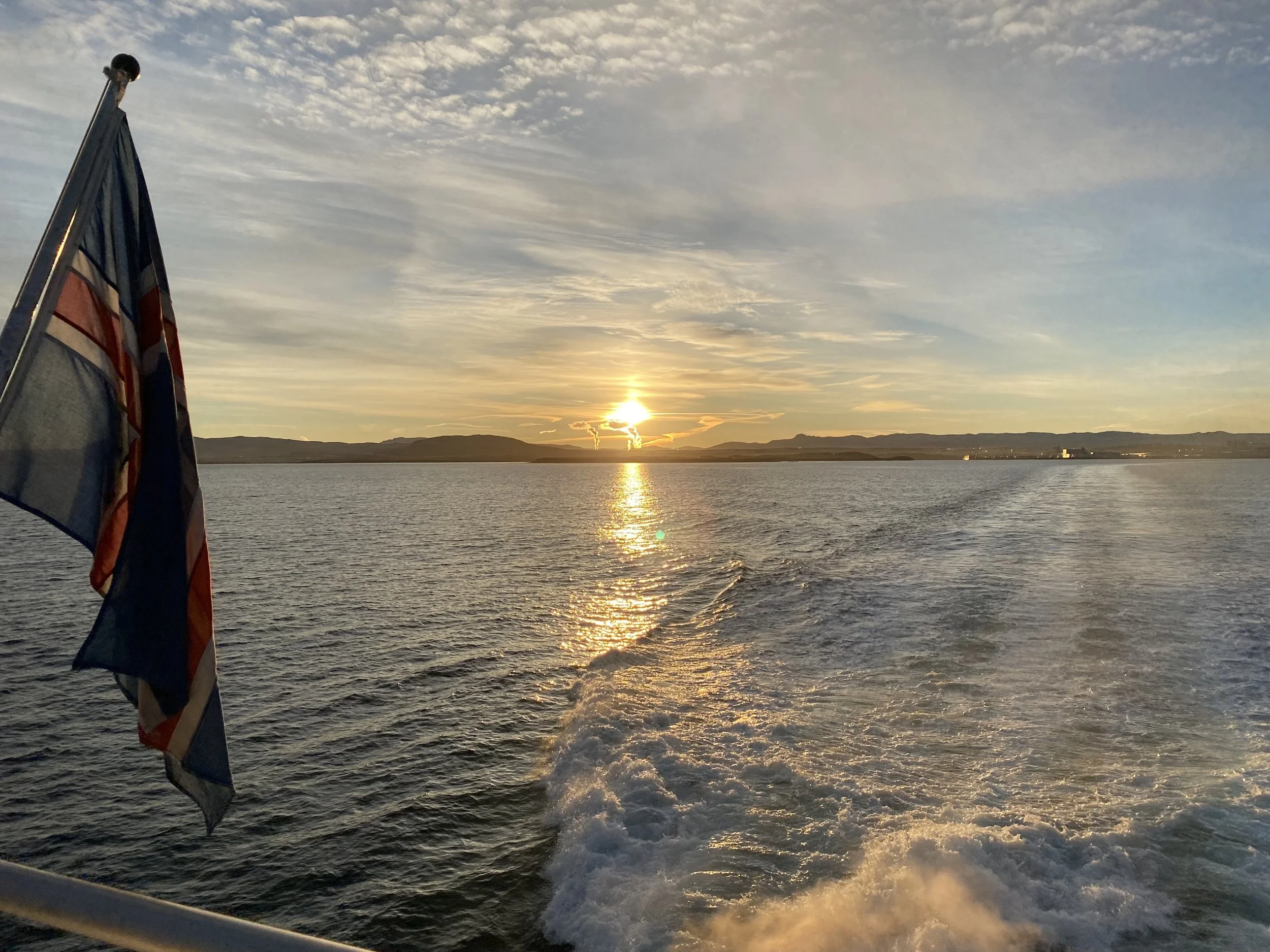  The sun begins to rise over Rekjavik, seen from the back of a whale watching boat it glints off the sea and the wake of the boat. 