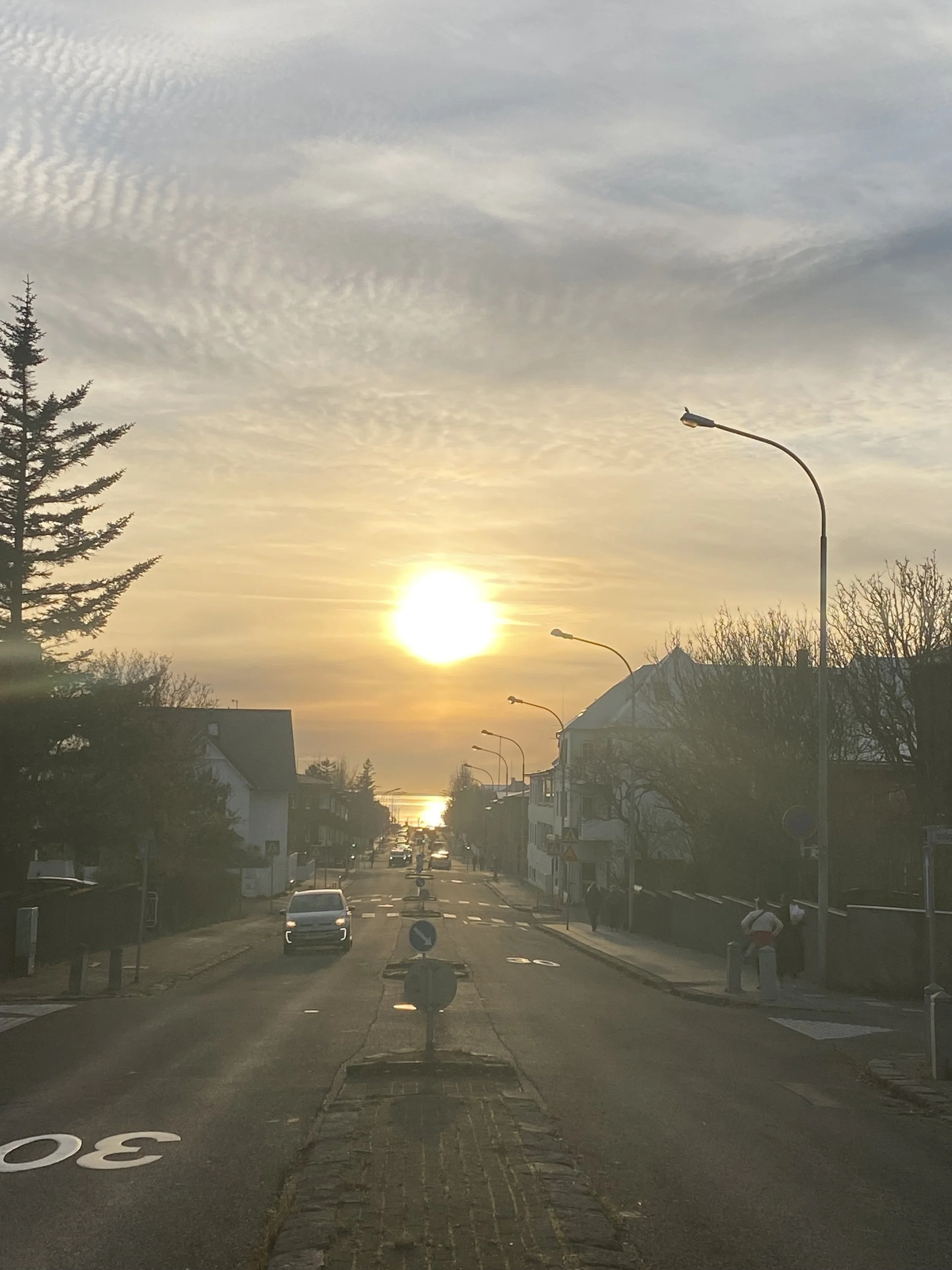  The sun is setting over the sea in Rekjavik, the clouds around it have turned peach and the light is reflected over the sea. 