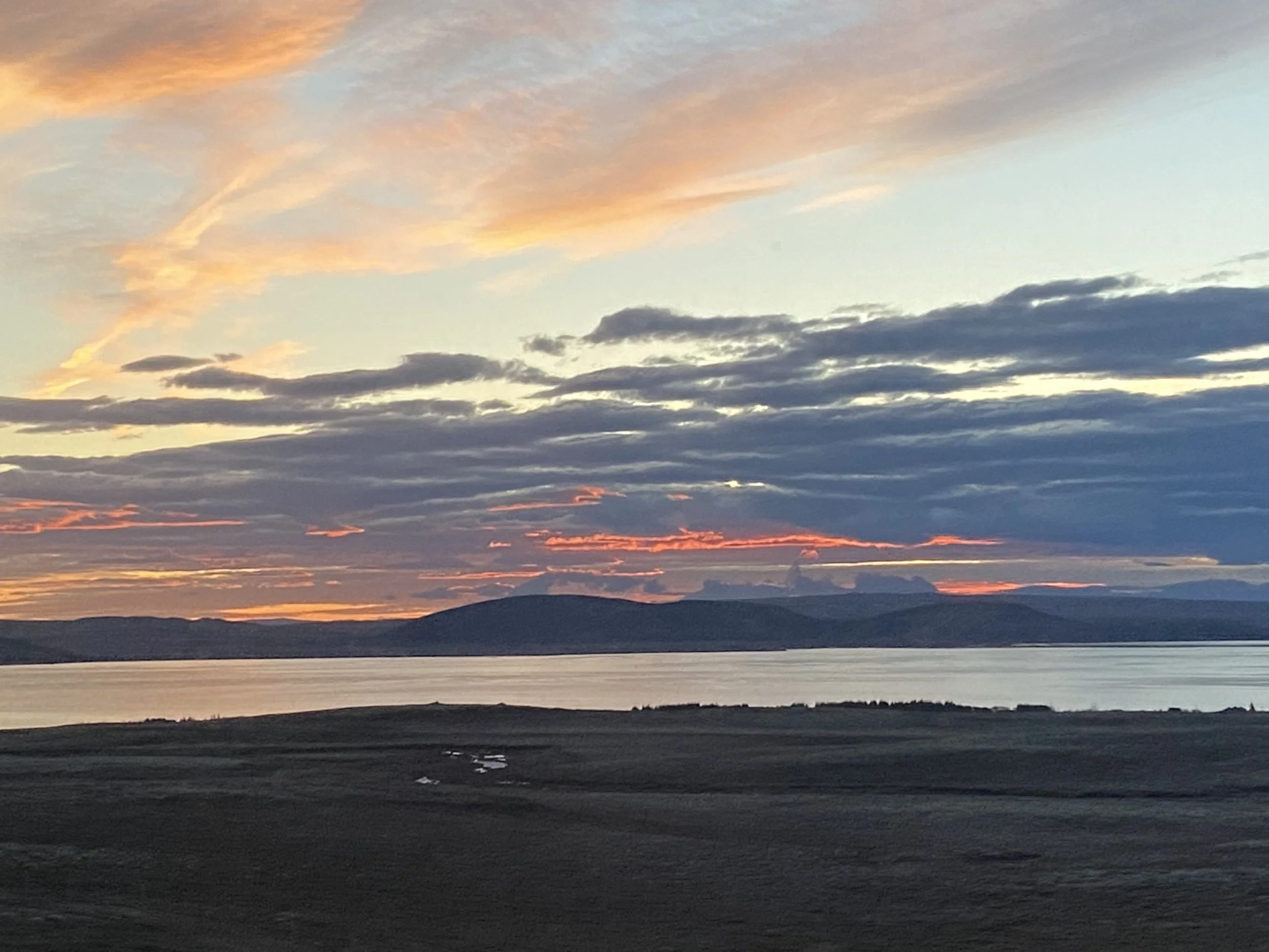 The sun rises over mountains in Iceland near Rekjavik.  The clouds create a series of bumpy stripes which are illuminated bright pink against the grey. 