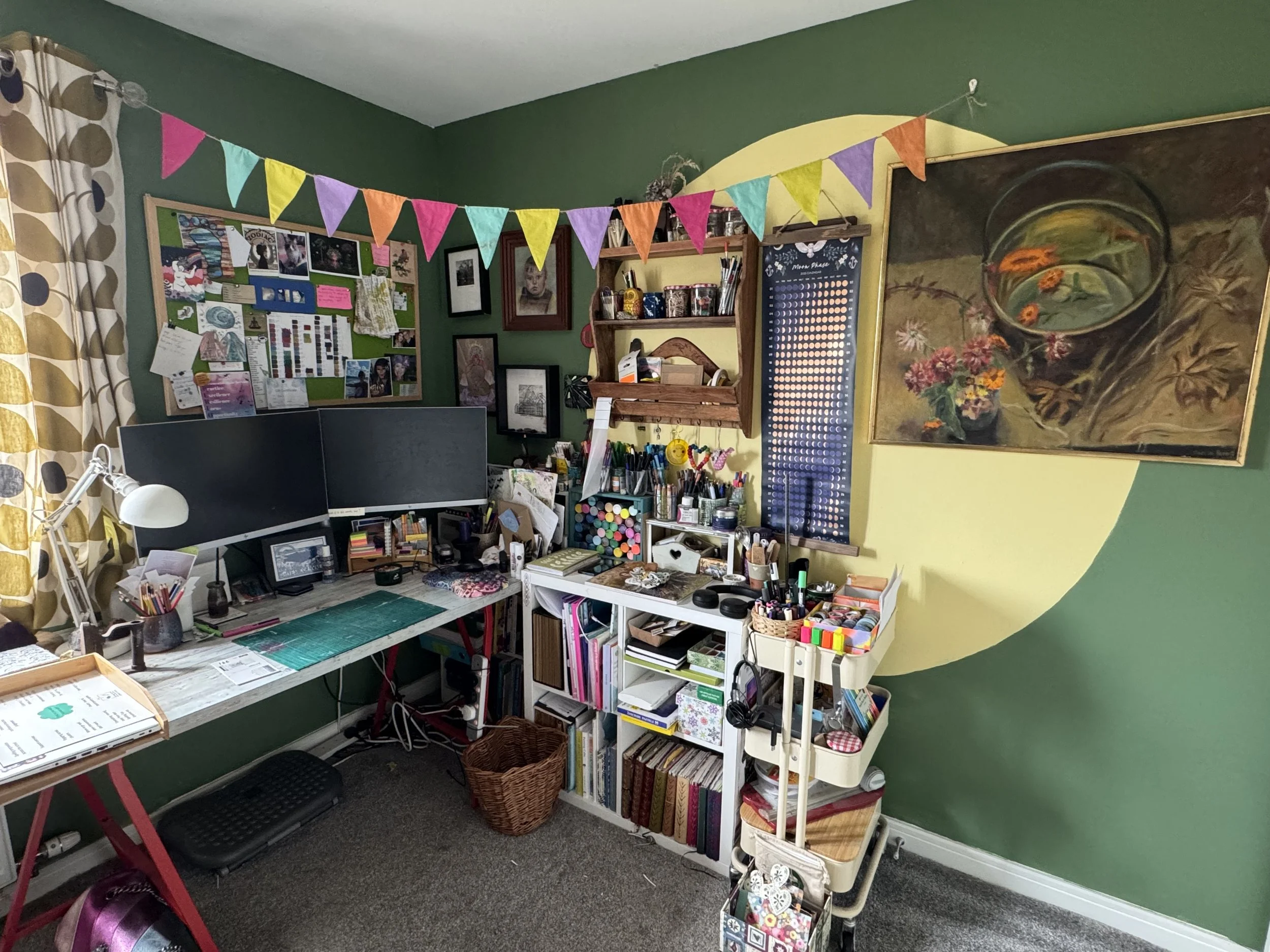 Creative home office with green walls, a large desk, art supplies, and colourful bunting.