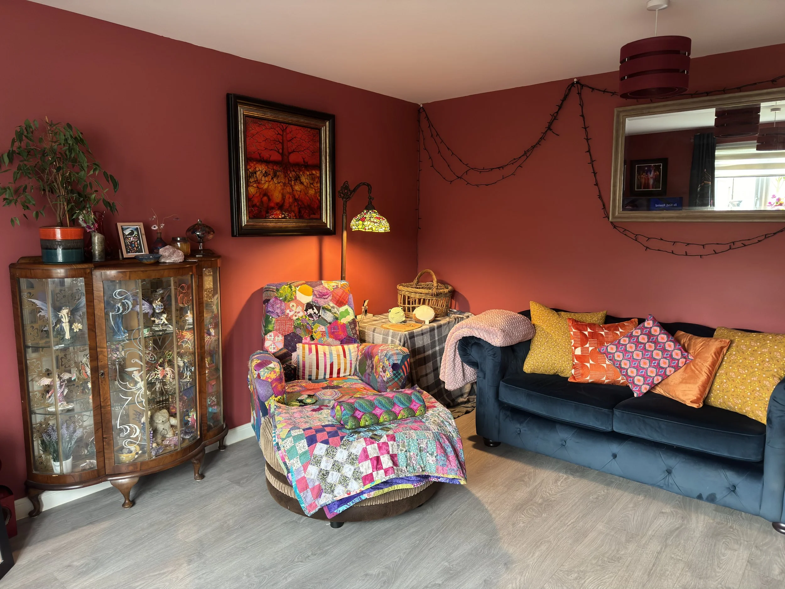 Cosy living room with rich red walls, a blue sofa, and a colourful patchwork armchair