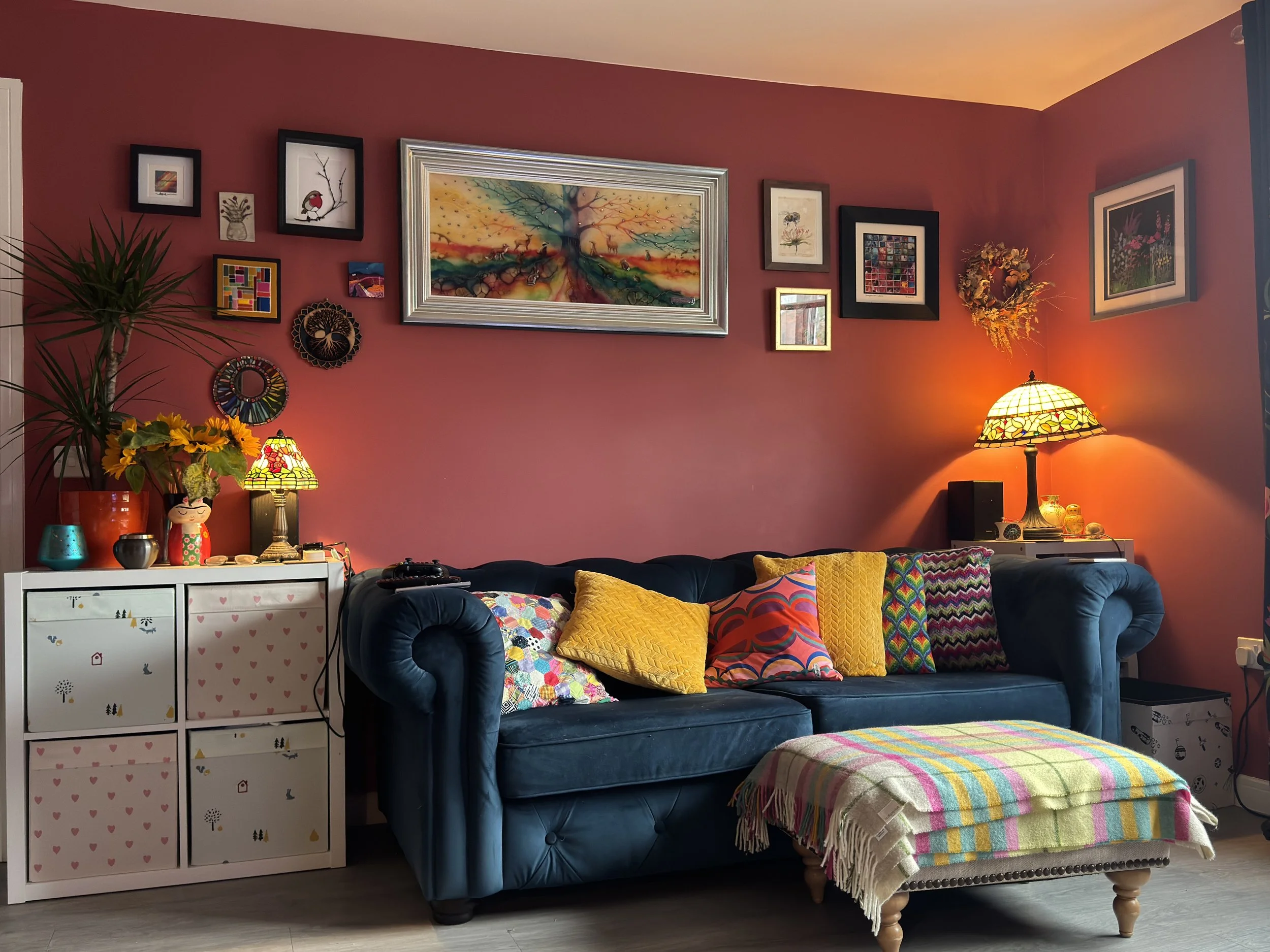 Living room with rich red walls, a blue sofa, framed art, and colourful cushions.