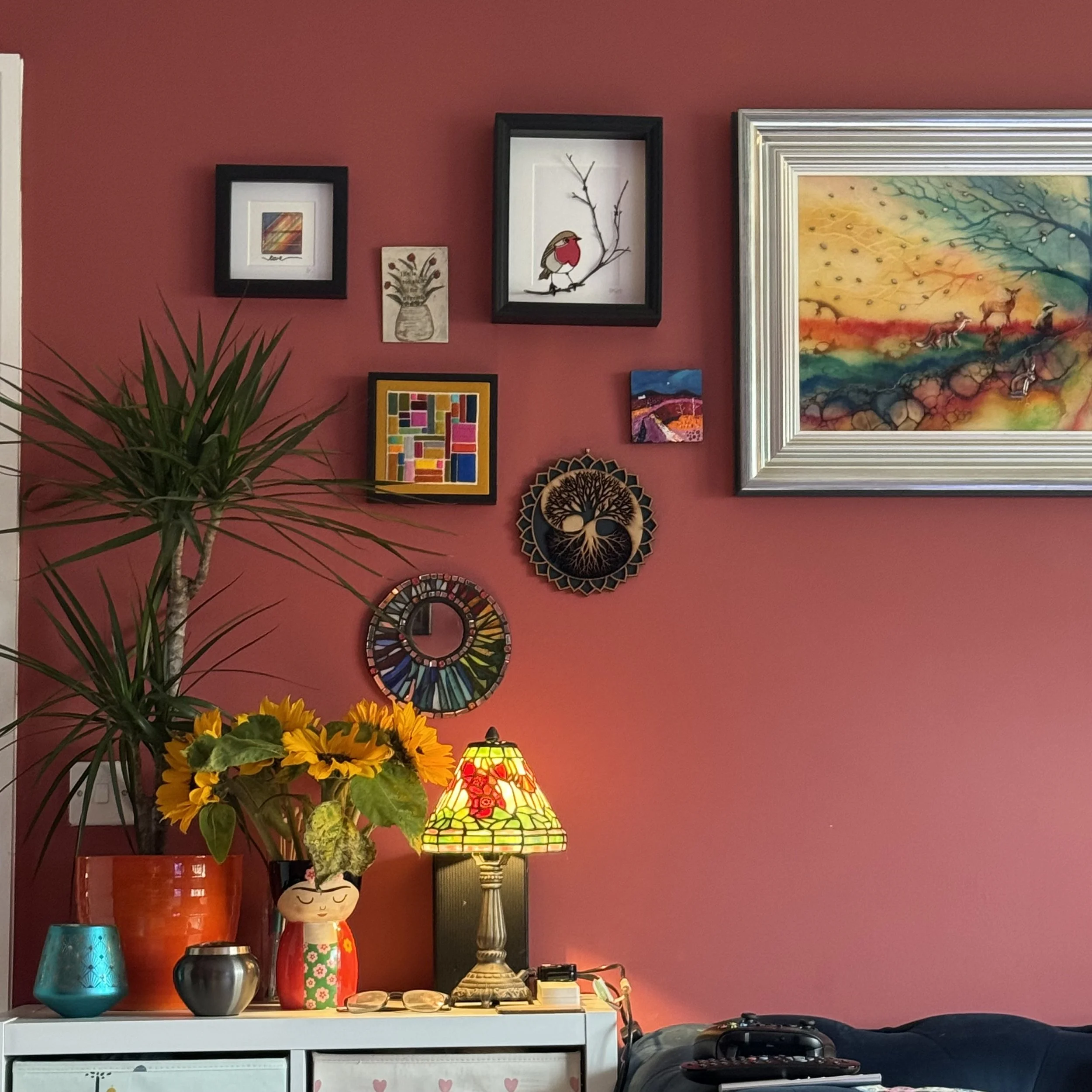 Close-up of a red wall adorned with various framed artworks, a large plant, and a colourful lamp